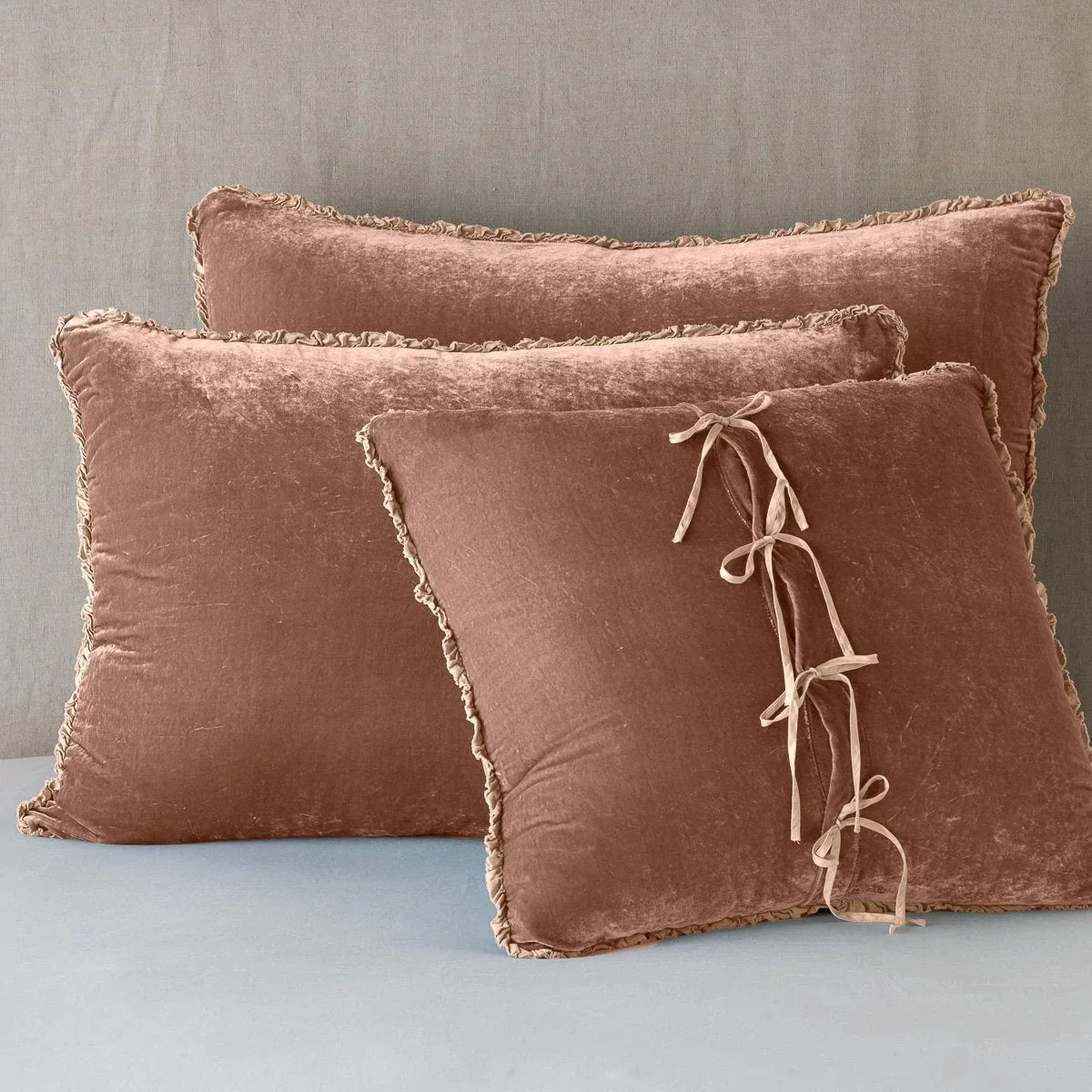 Rouge: Silk velvet shams with a petite ruffle leaning upright against a neutral headboard. The front sham is backwards, showcasing the charmeuse tie closures.