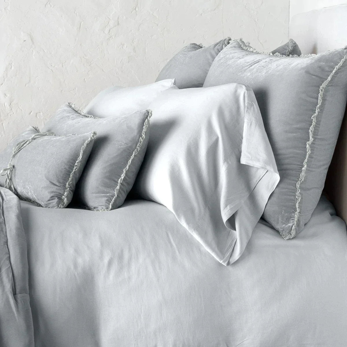 : Carmen shams in sterling on monochromatic bed, leaning upright behind sleeping and throw pillows. Close-up side view showcases the charmeuse petite raw-edge ruffle.