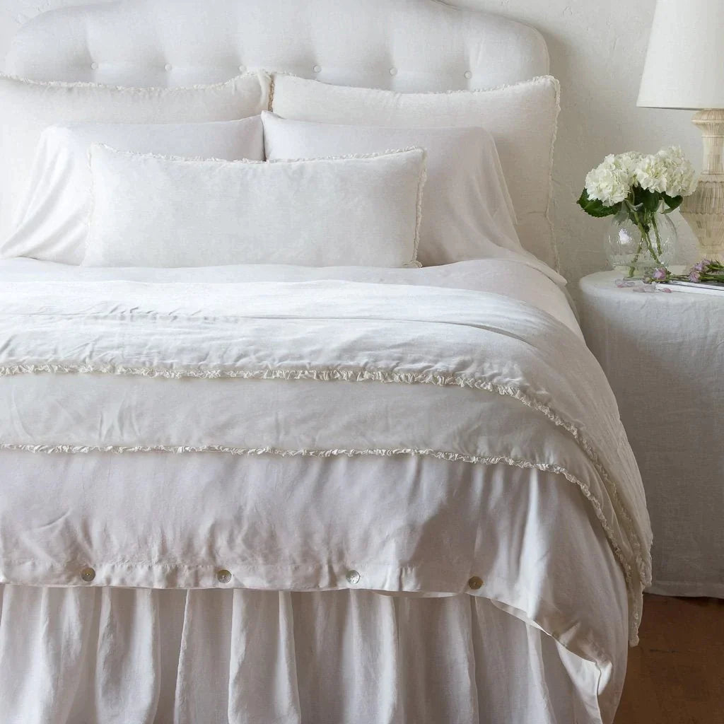 : Carmen shams in winter white on a monochromatic bed, stacked behind sleeping and throw pillows - view from end of bed.