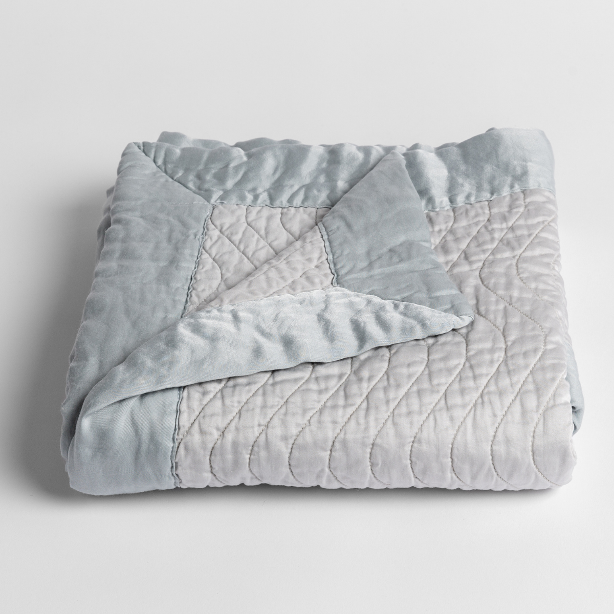Cloud: a folded quilted cotton sateen baby blanket with its corner folded down to show the trim contrast - shot against a white background.