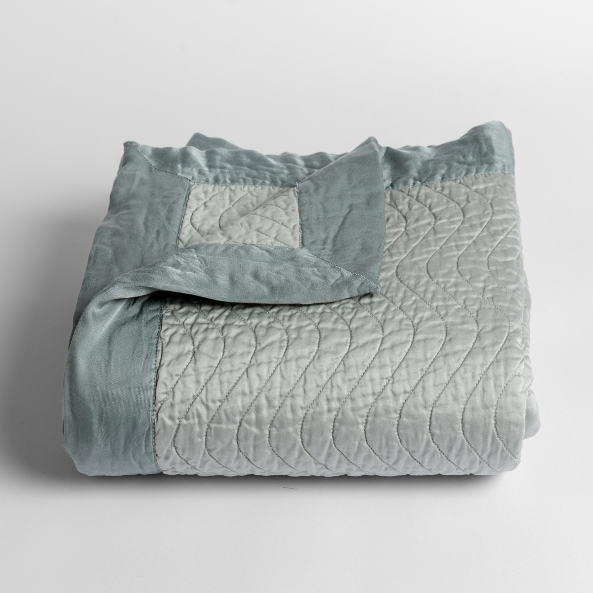 Eucalyptus: a folded quilted cotton sateen baby blanket with its corner folded down to show the trim contrast - shot against a white background.