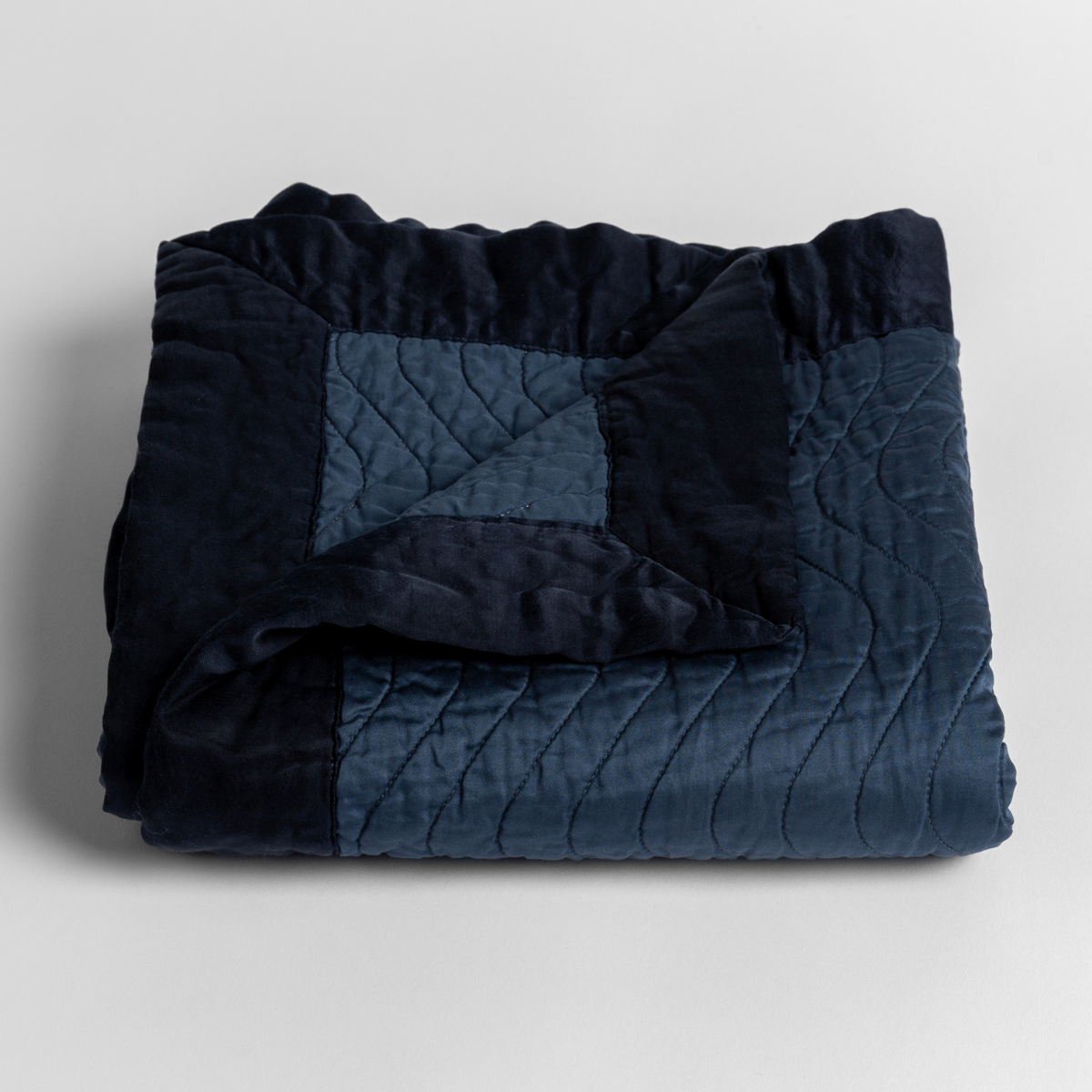 Midnight: a folded quilted cotton sateen baby blanket with its corner folded down to show the trim contrast - shot against a white background.