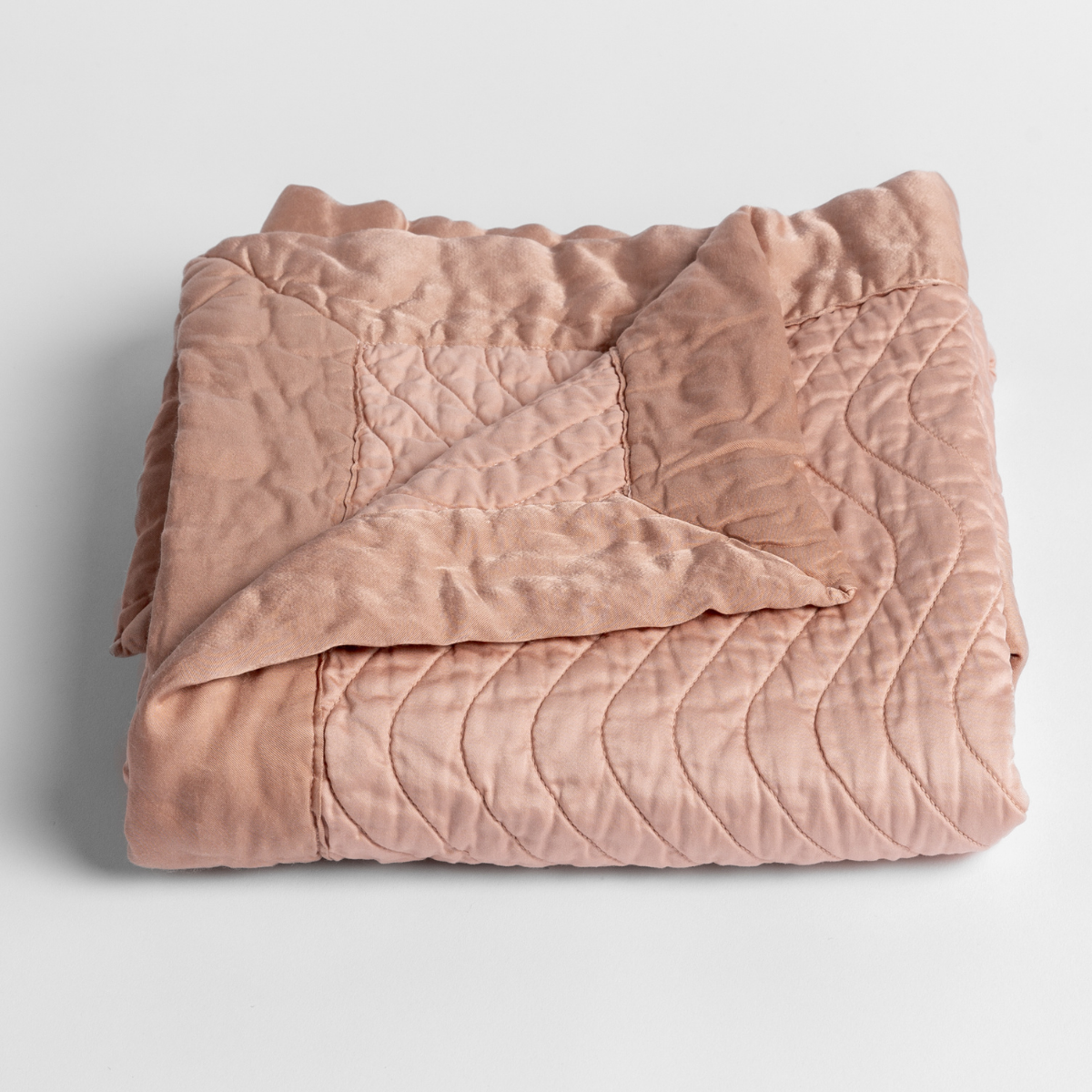 Rouge: a folded quilted cotton sateen baby blanket with its corner folded down to show the trim contrast - shot against a white background.