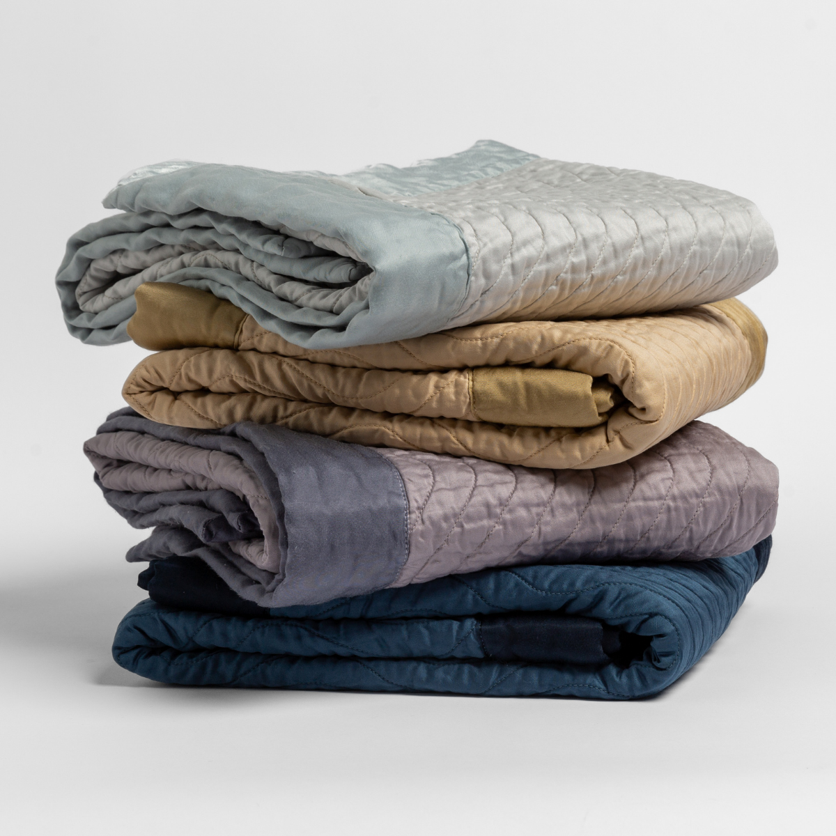 : stack of 4 quilted cotton sateen baby blankets in cloud, honeycomb, French Lavender and Midnight.
