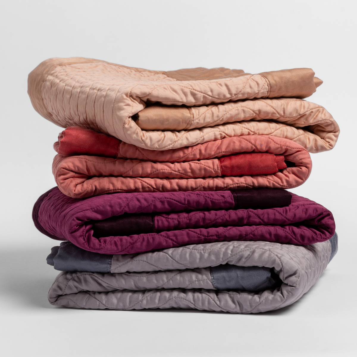 : stack of quilted cotton sateen baby blankets in Rouge, Poppy, fig and french lavender