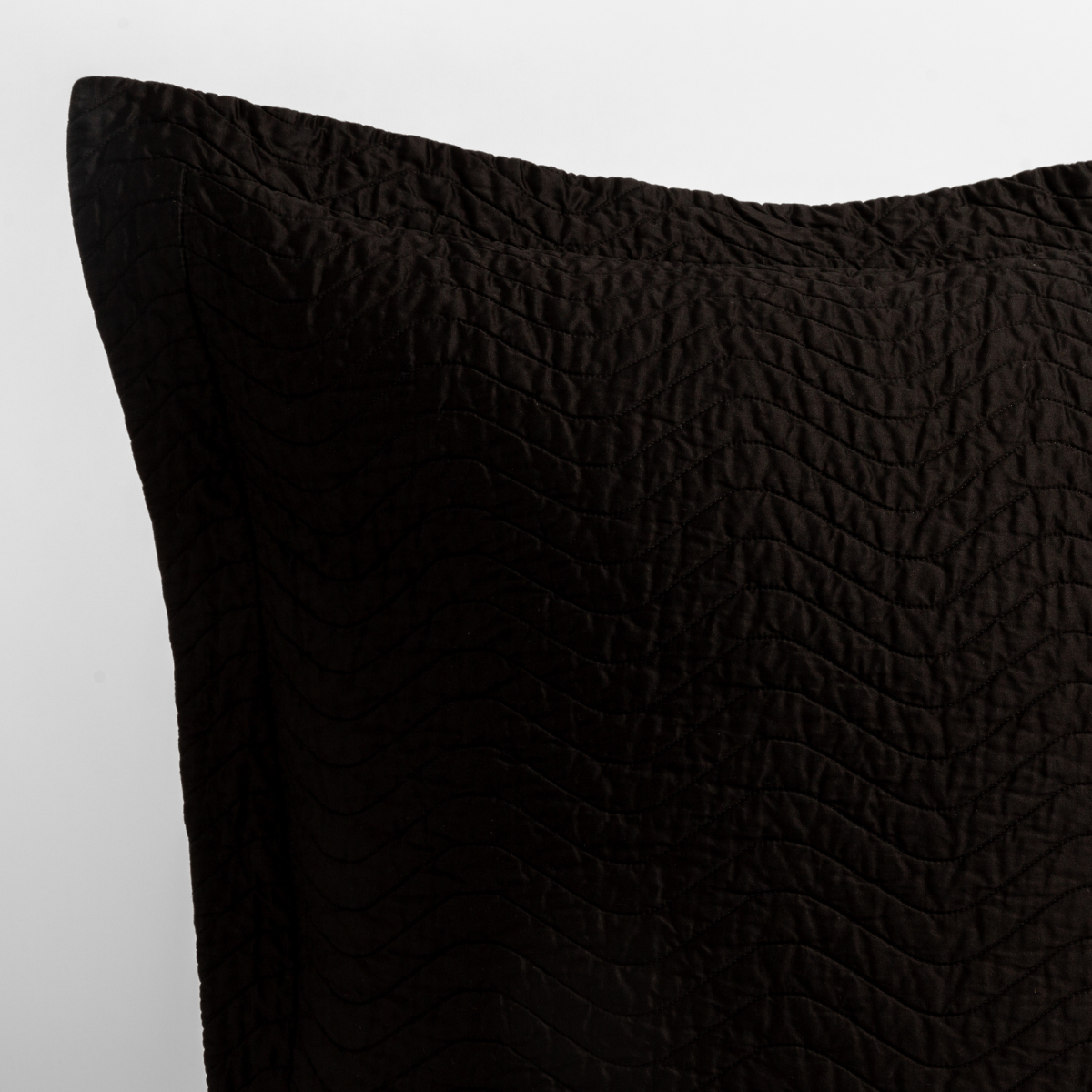 Corvino: a close up of a pillow corner showing the flange framing quilted cotton sateen shot against a white background.