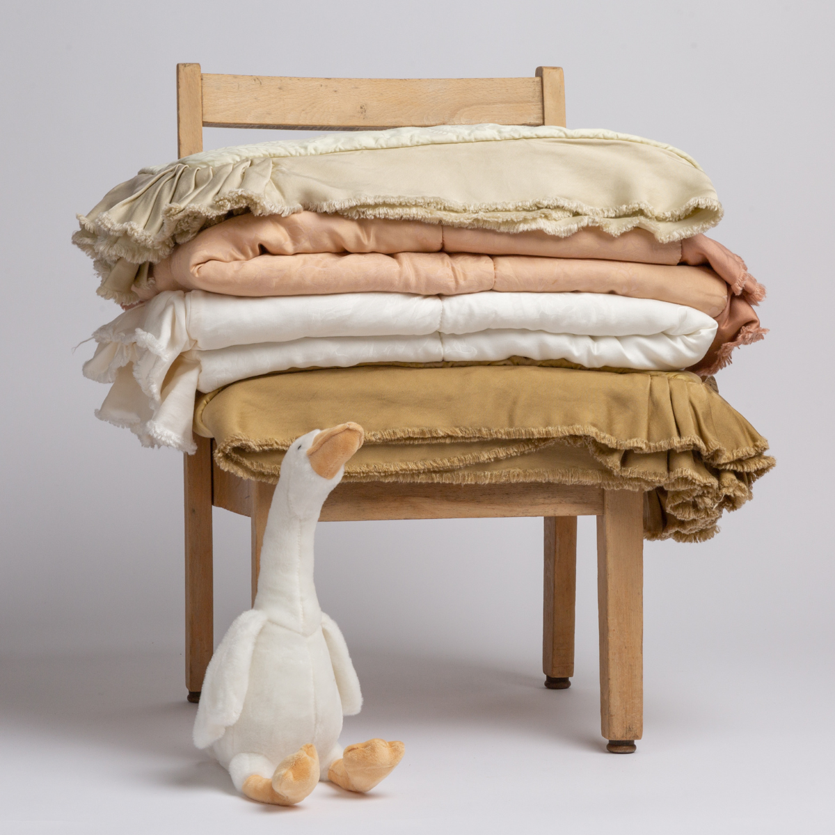 : stack of Mirabella Baby Blankets on a child-sized chair with a stuffed duck at the foot of one of the chair's legs - shot against a plain white background.