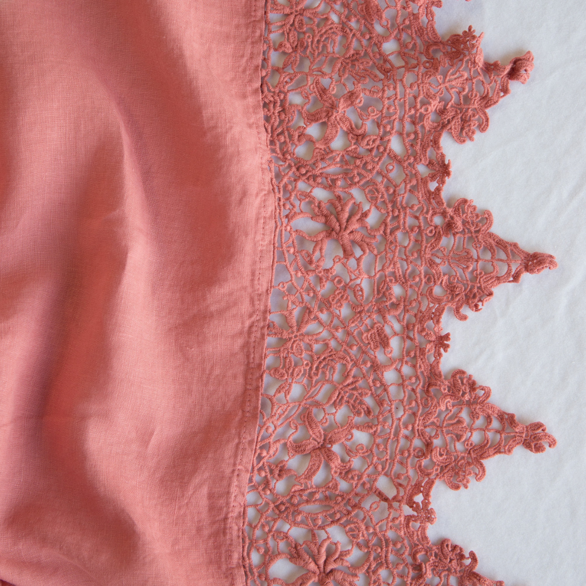 Poppy: A close up of Frida, an antique cotton lace trim on a linen body, shown in poppy, a warm coral pink.