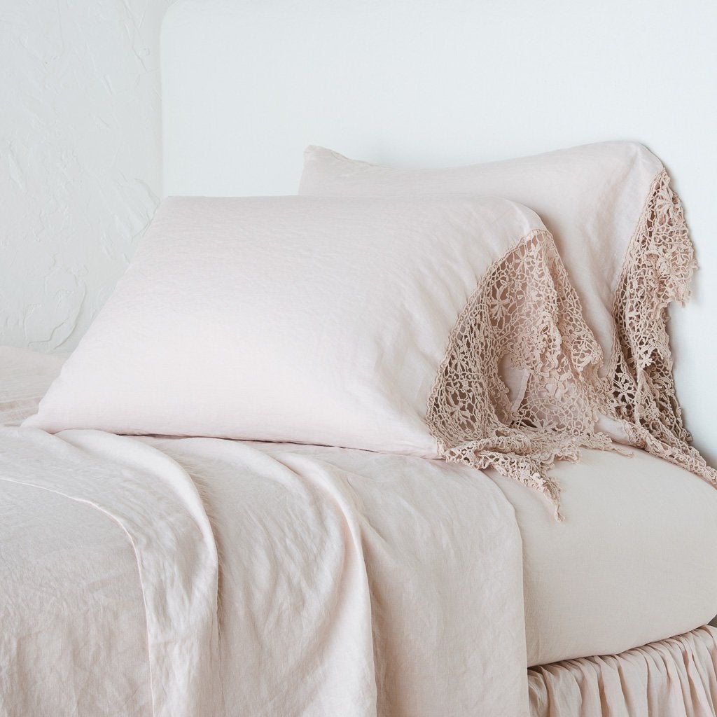 : Frida pillowcases leaning against a plain wall on a monochromatic pearl bed - cropped three-quarter angle.