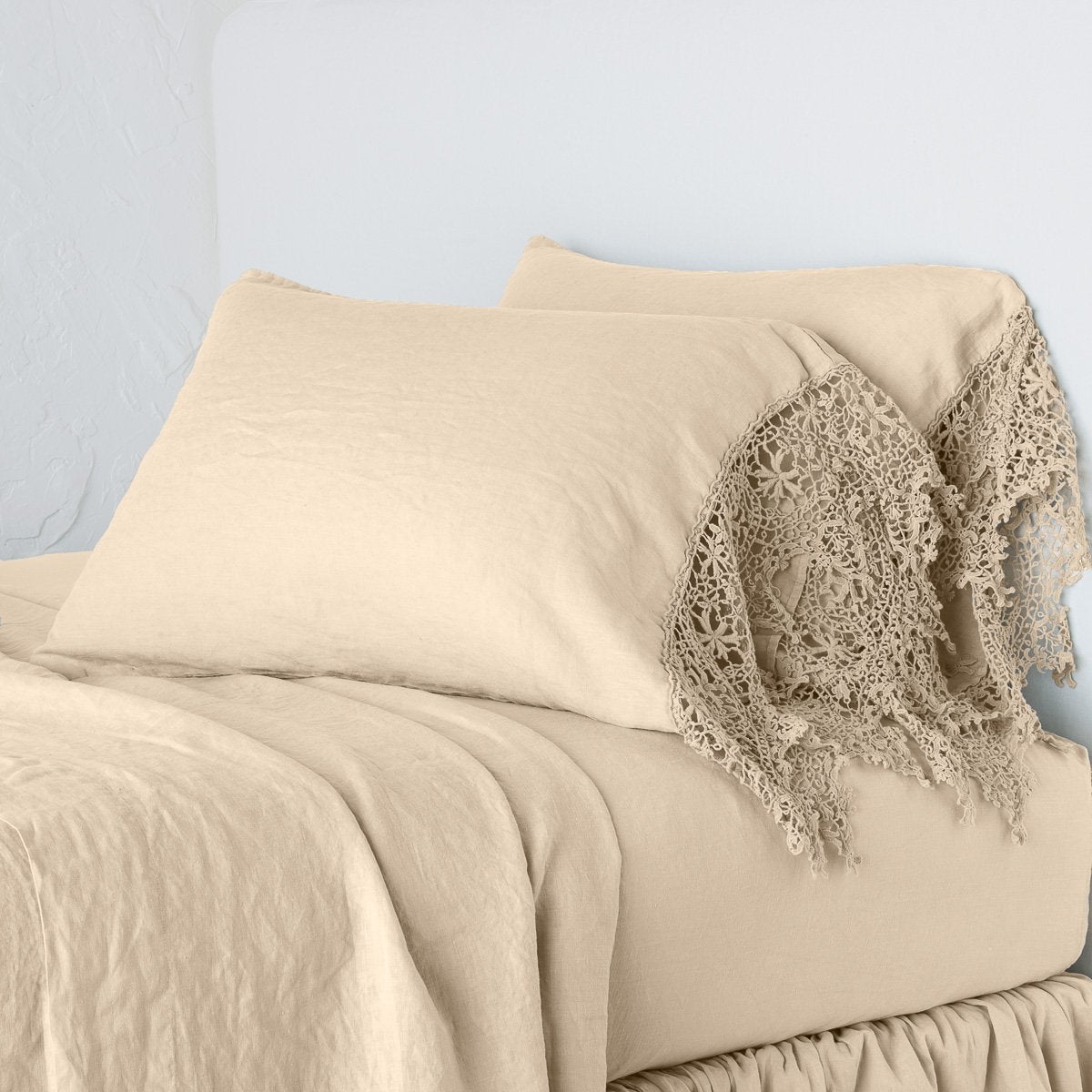 Honeycomb: Lace trimmed linen pillowcases leaning against a plain wall on a monochromatic bed - cropped three-quarter angle.