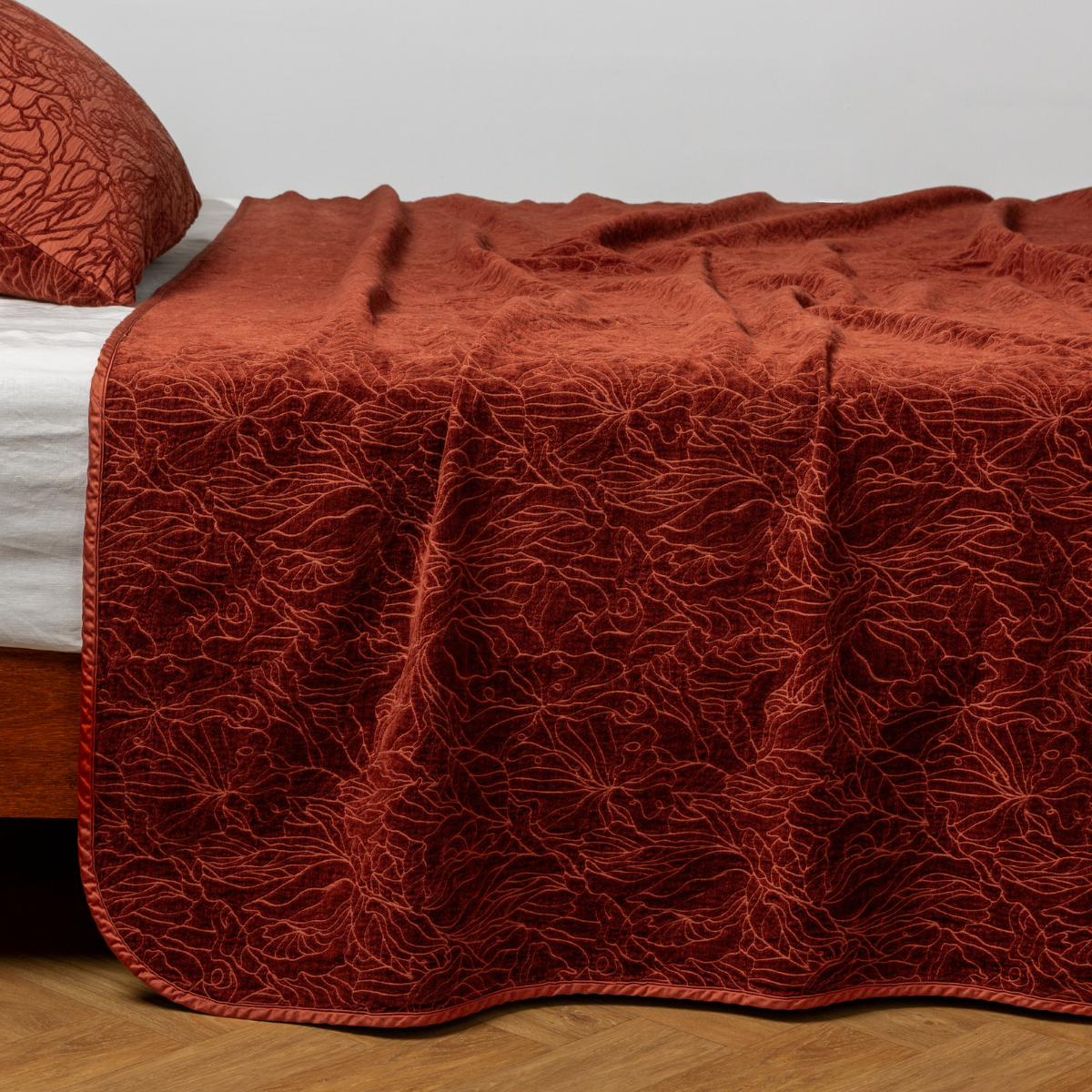 Autumn: A close-up side view of a bed with our Georgia Bedspread on its chenille jacquard side and a matching pillowcase on its cotton jacquard side in Autumn, a rich terracotta tone.