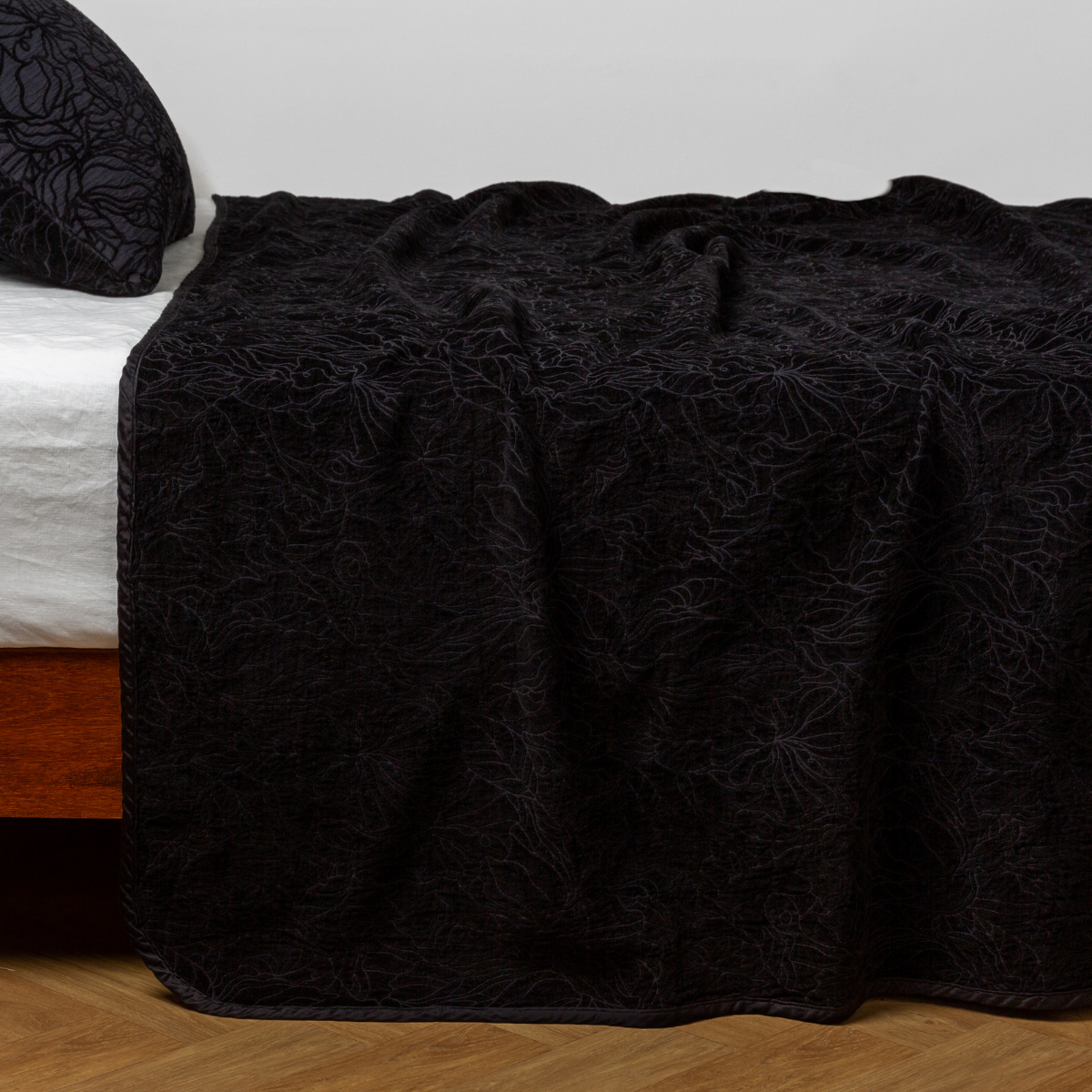 Corvino: side view of the chenille jacquard side of a bedspread with the cotton jacquard side showing on the matching sham β shown with a winter white fitted sheet.