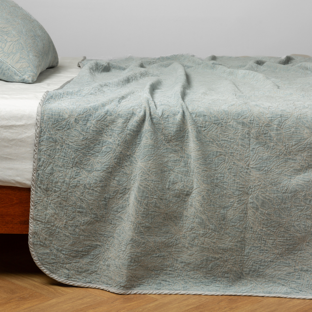 Eucalyptus: side view of the chenille jacquard side of a bedspread with the cotton jacquard side showing on the matching sham β shown with a winter white fitted sheet.