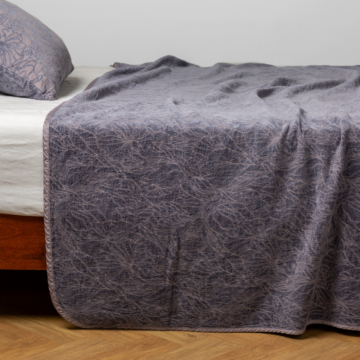 French Lavender: side view of the chenille jacquard side of a bedspread with the cotton jacquard side showing on the matching sham β shown with a winter white fitted sheet.