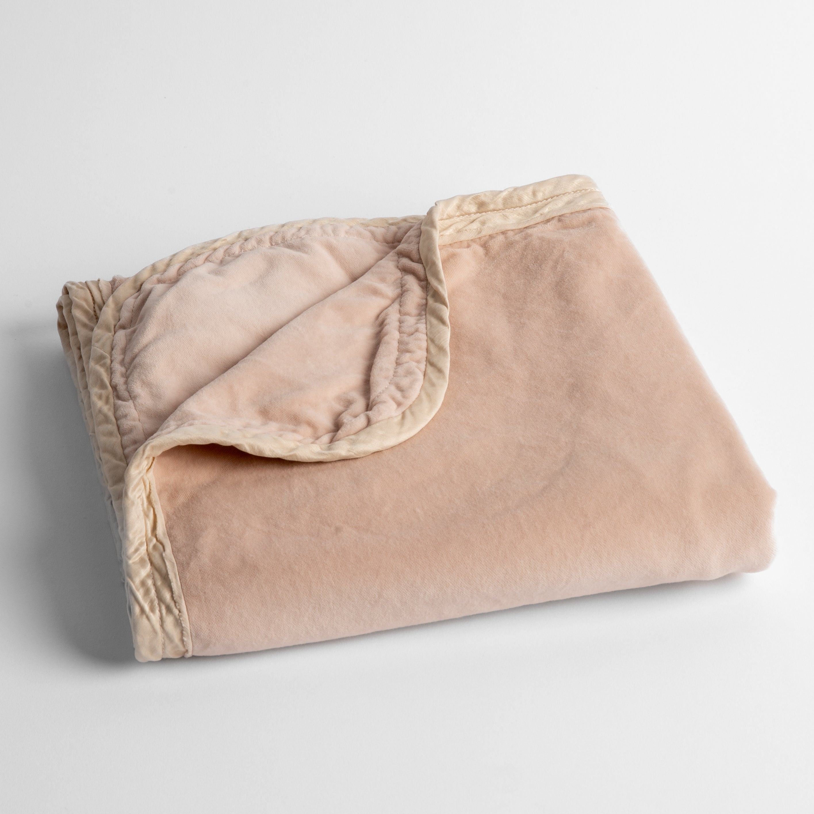 Pearl: cotton velvet baby blanket trimmed with charmeuse, folded with a covern folded back to show trim contrast; shot overhead and at a slight angle against a white background.