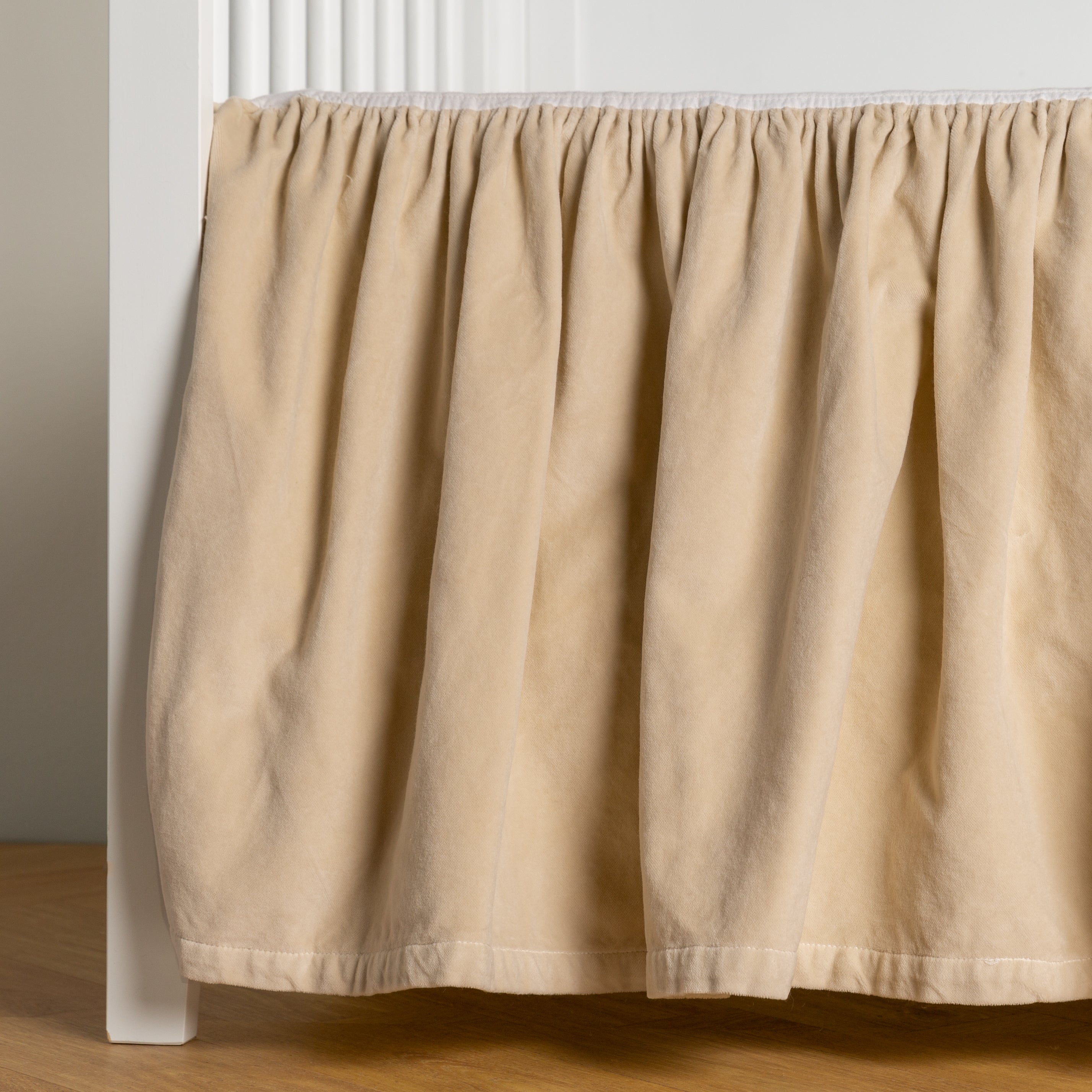 Parchment: cotton velvet crib skirt shown on a white crib .
