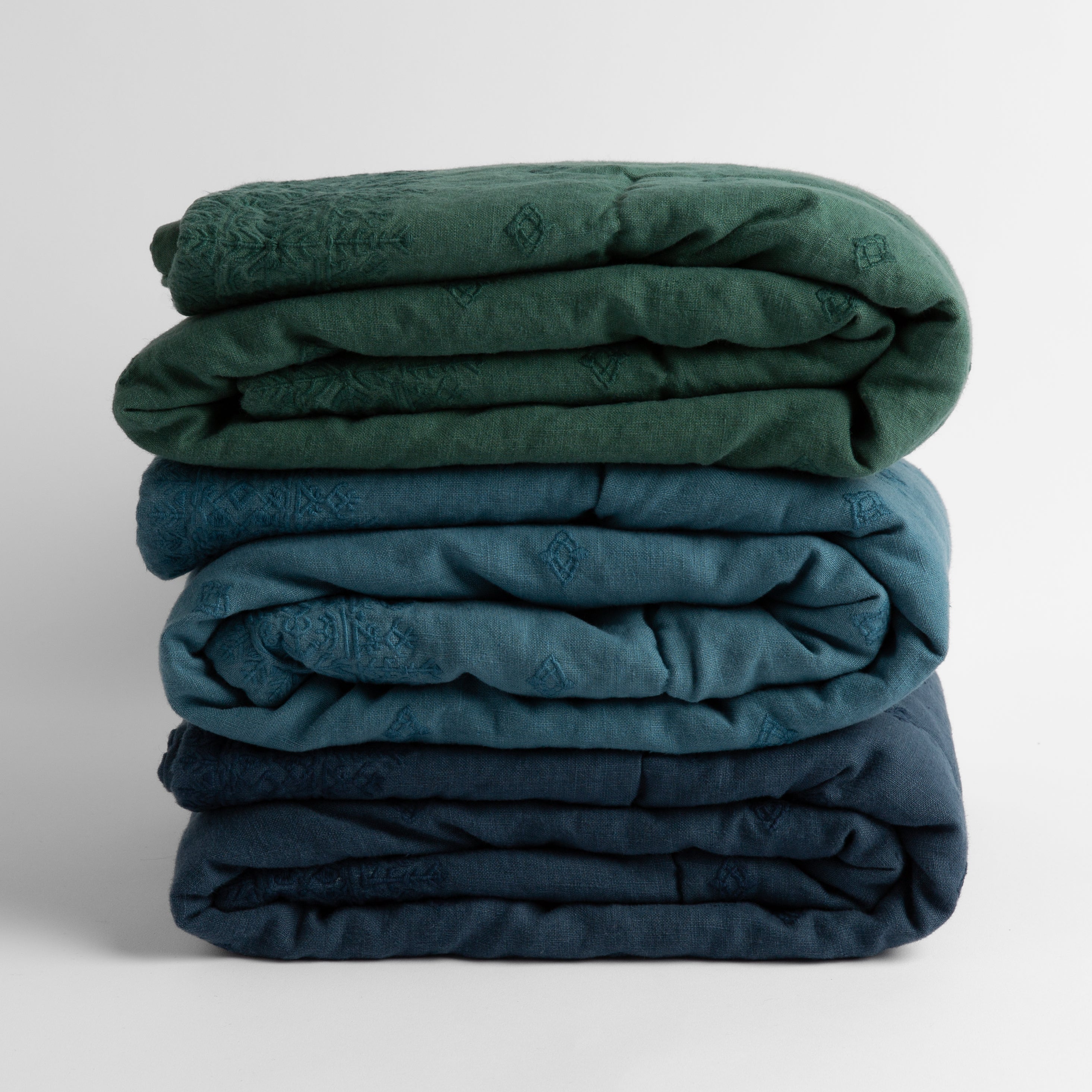 a stack of three embroidered linen baby blankets in jade, cenote and midnight