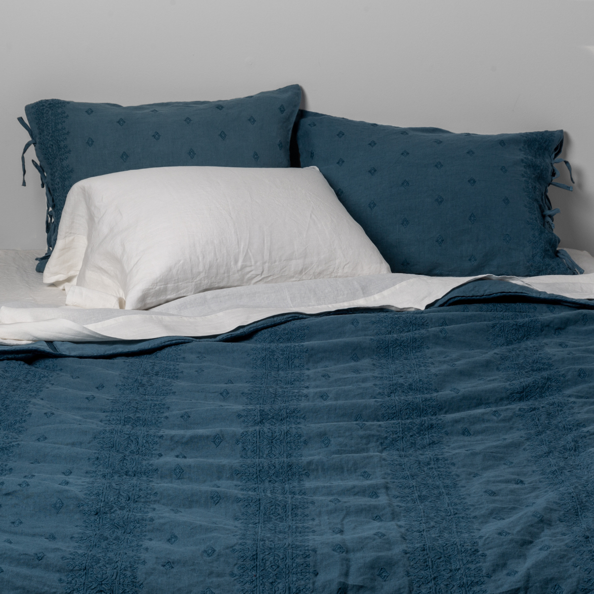Cenote: Bedspread with matching shams on a bed with white sheets and sleeping pillows. Shot from the end of bed view, the flat sheet is pulled back over the top of the bedspread.