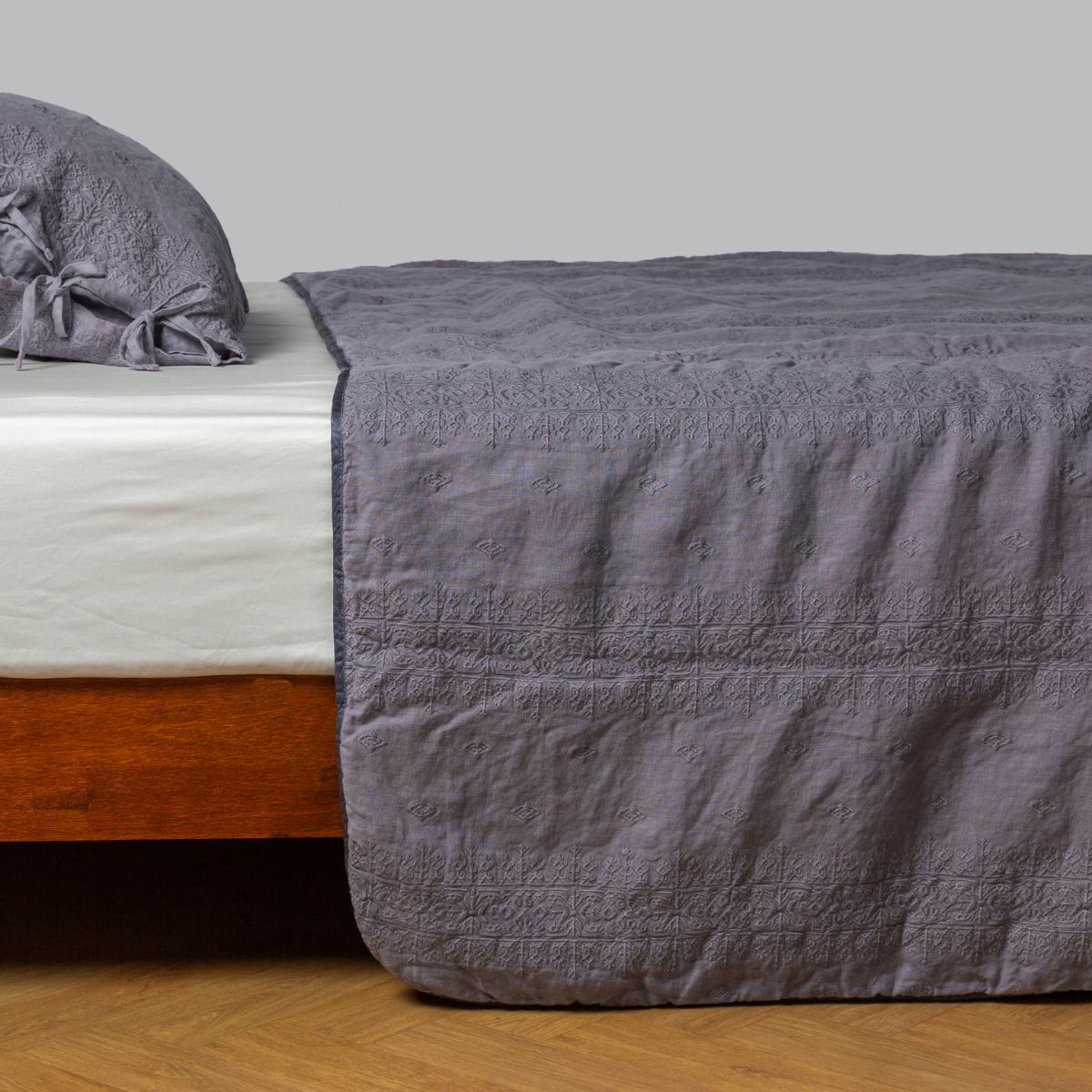 French Lavender: embroidered midweight linen bedspread with matching sham on a bed with a white fitted sheet. shot from the side view, the bedframe is slightly visible against a white background and medium wood floor.