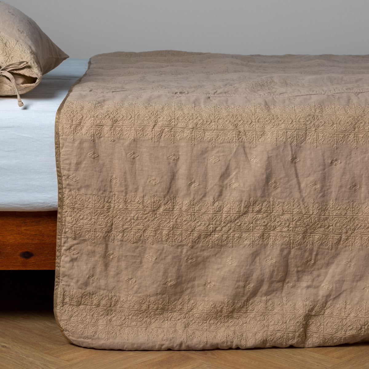 Honeycomb: embroidered midweight linen bedspread with matching sham on a bed with a white fitted sheet. Shot from the side view, the bedframe is slightly visible against a white background and medium wood floor.