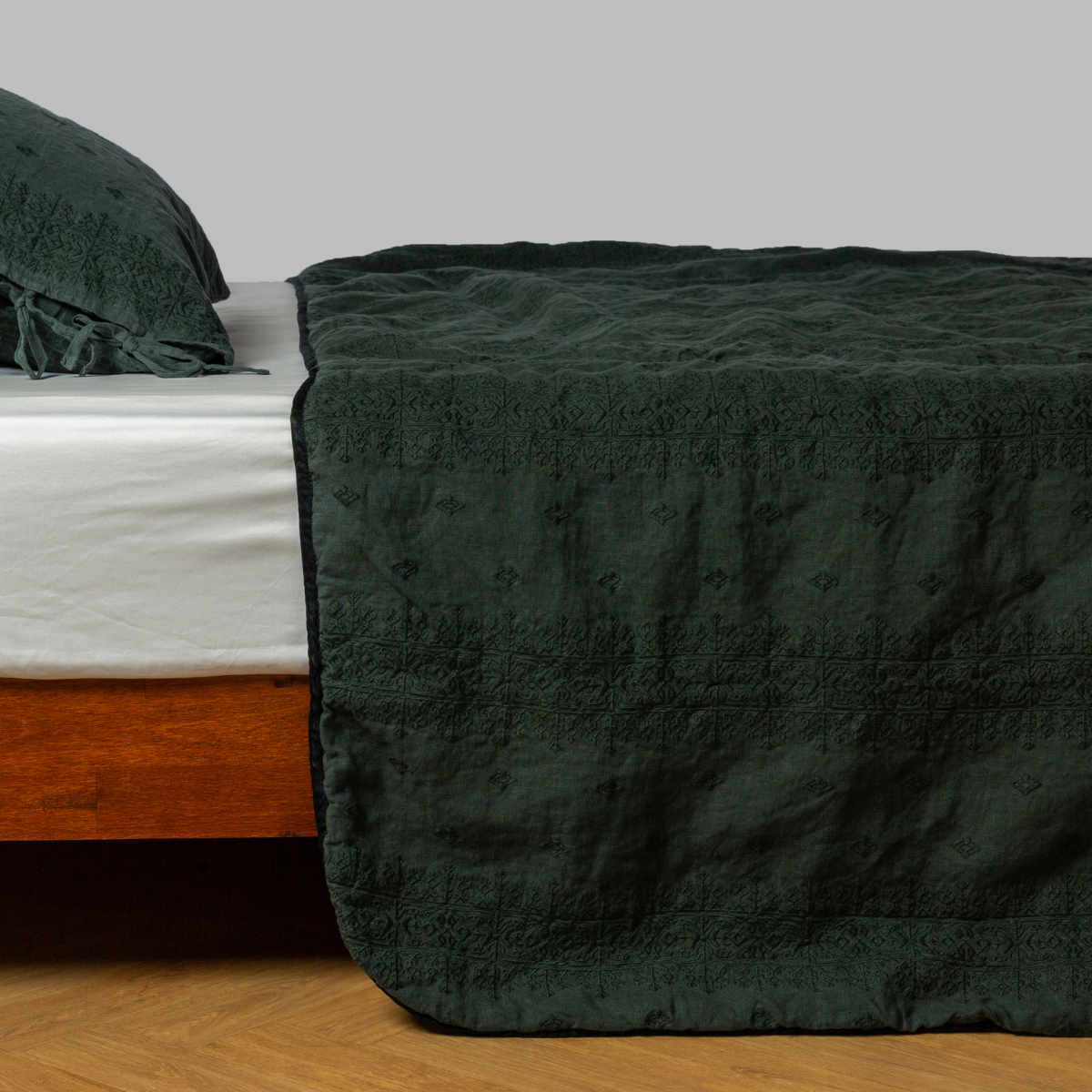 Juniper: embroidered midweight linen bedspread with matching sham on a bed with a white fitted sheet. shot from the side view, the bedframe is slightly visible against a white background and medium wood floor.