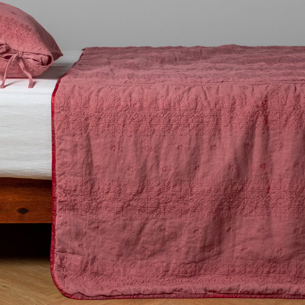 Poppy: embroidered midweight linen bedspread with matching sham on a bed with a white fitted sheet. Shot from the side view, the bedframe is slightly visible against a white background and medium wood floor.