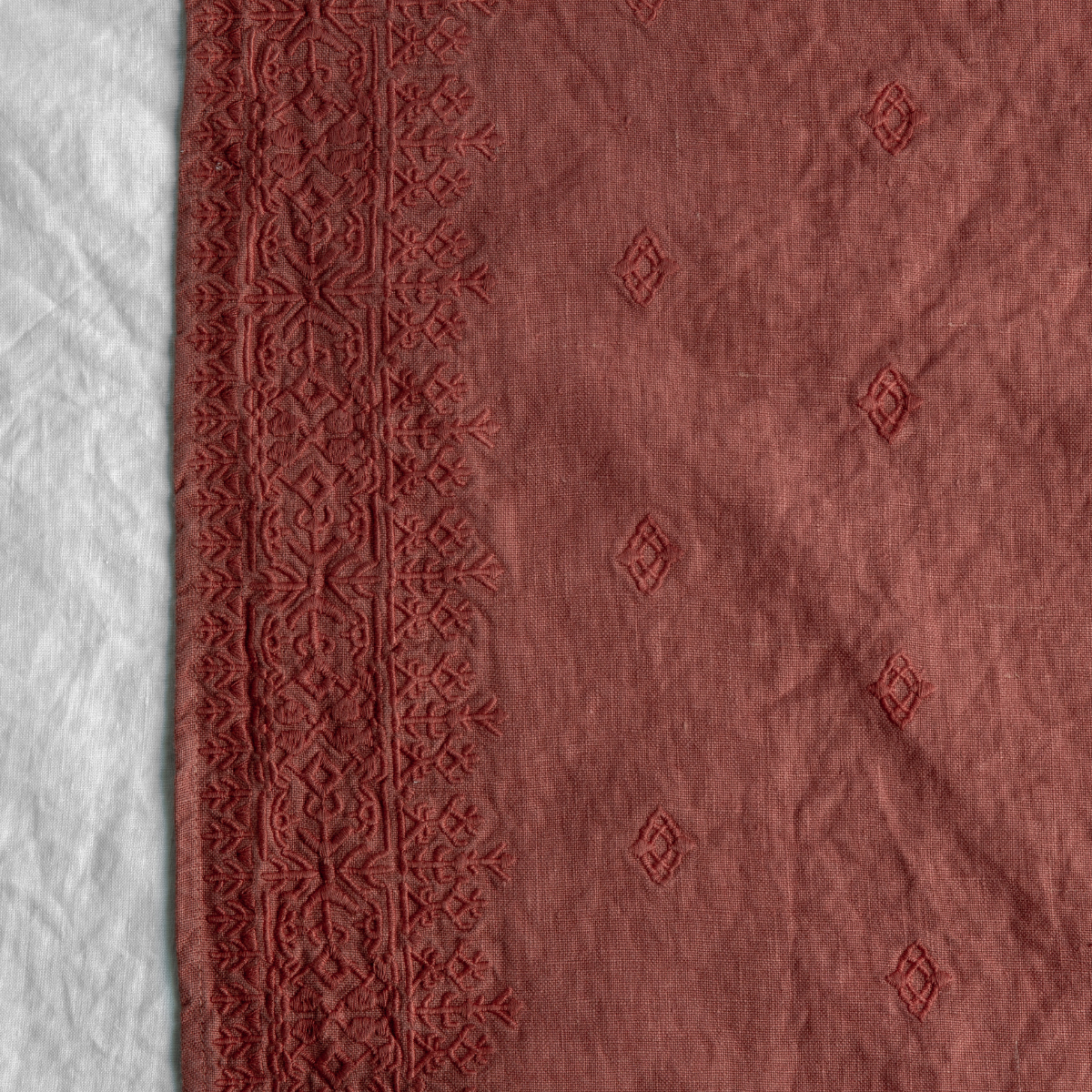 Poppy: A close up of Ines, midweight linen with cotton embroidery, in poppy, a warm coral pink.