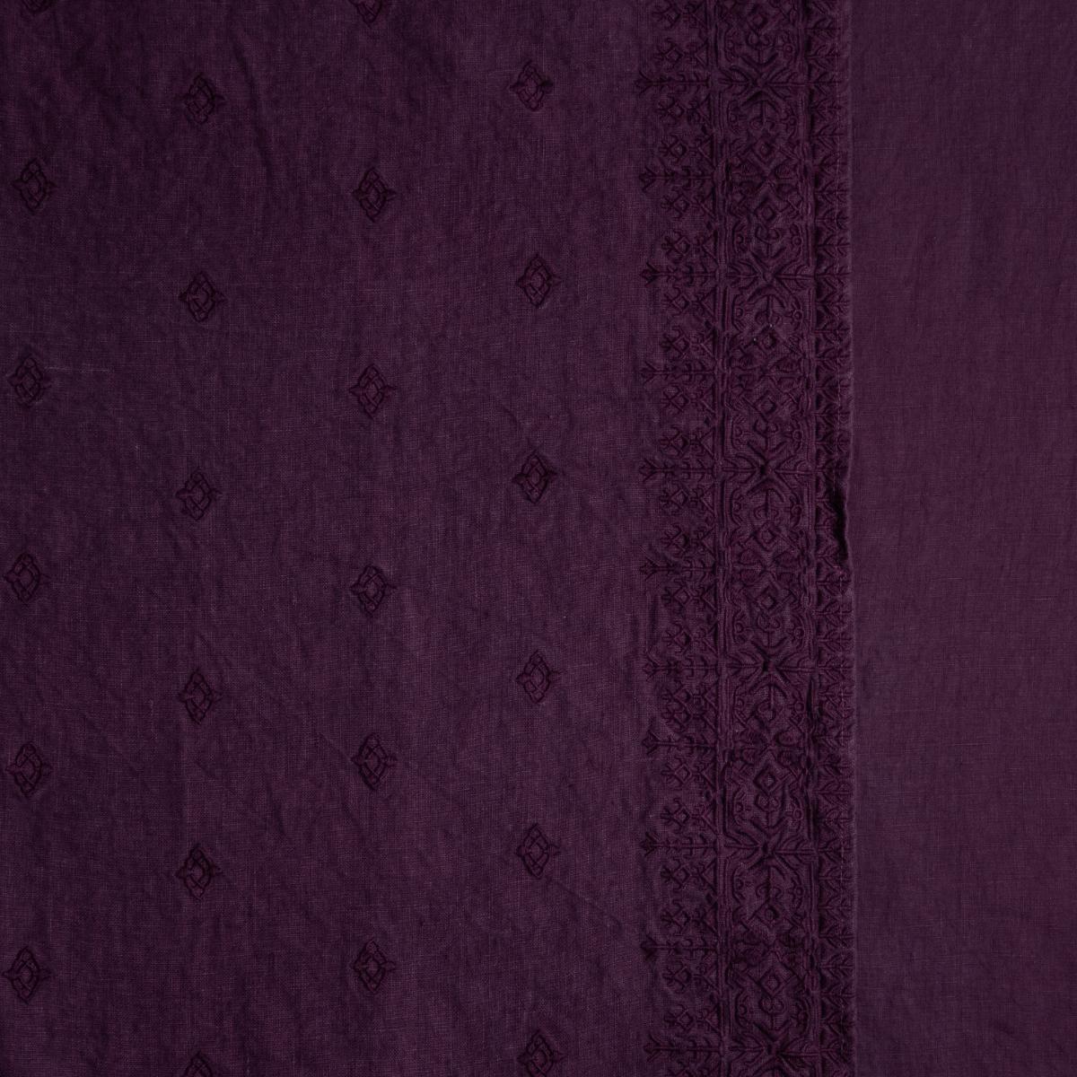Fig: A close up of embroidered midweight linen fabric in fig, a richly saturated purple-garnet.