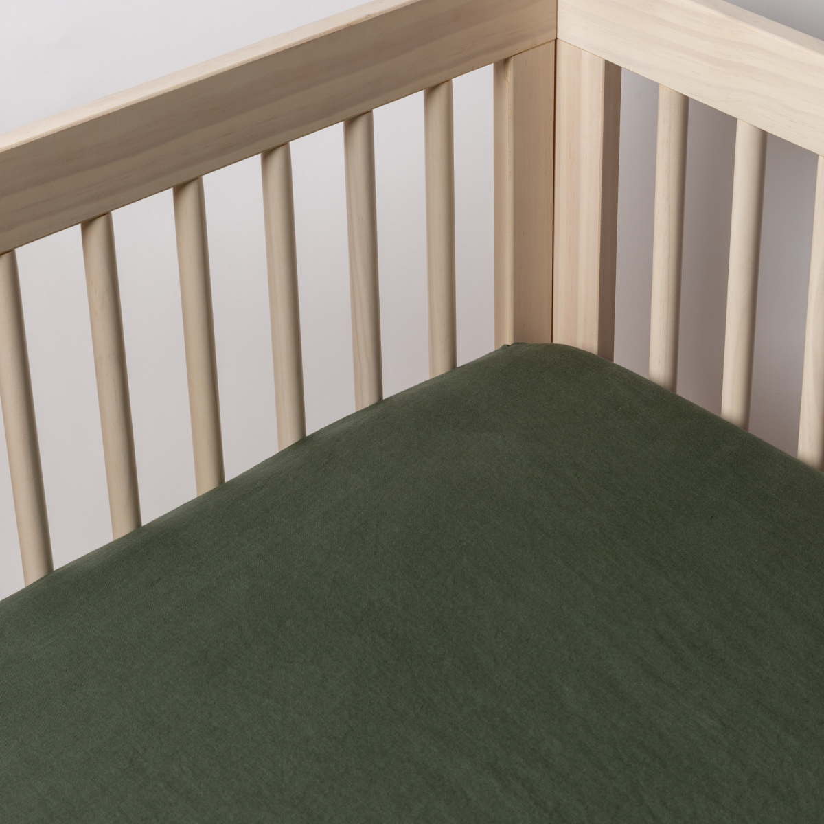 Juniper: linen crib sheet shown on a crib mattress shot slightly overhead into the inside corner of the crib.