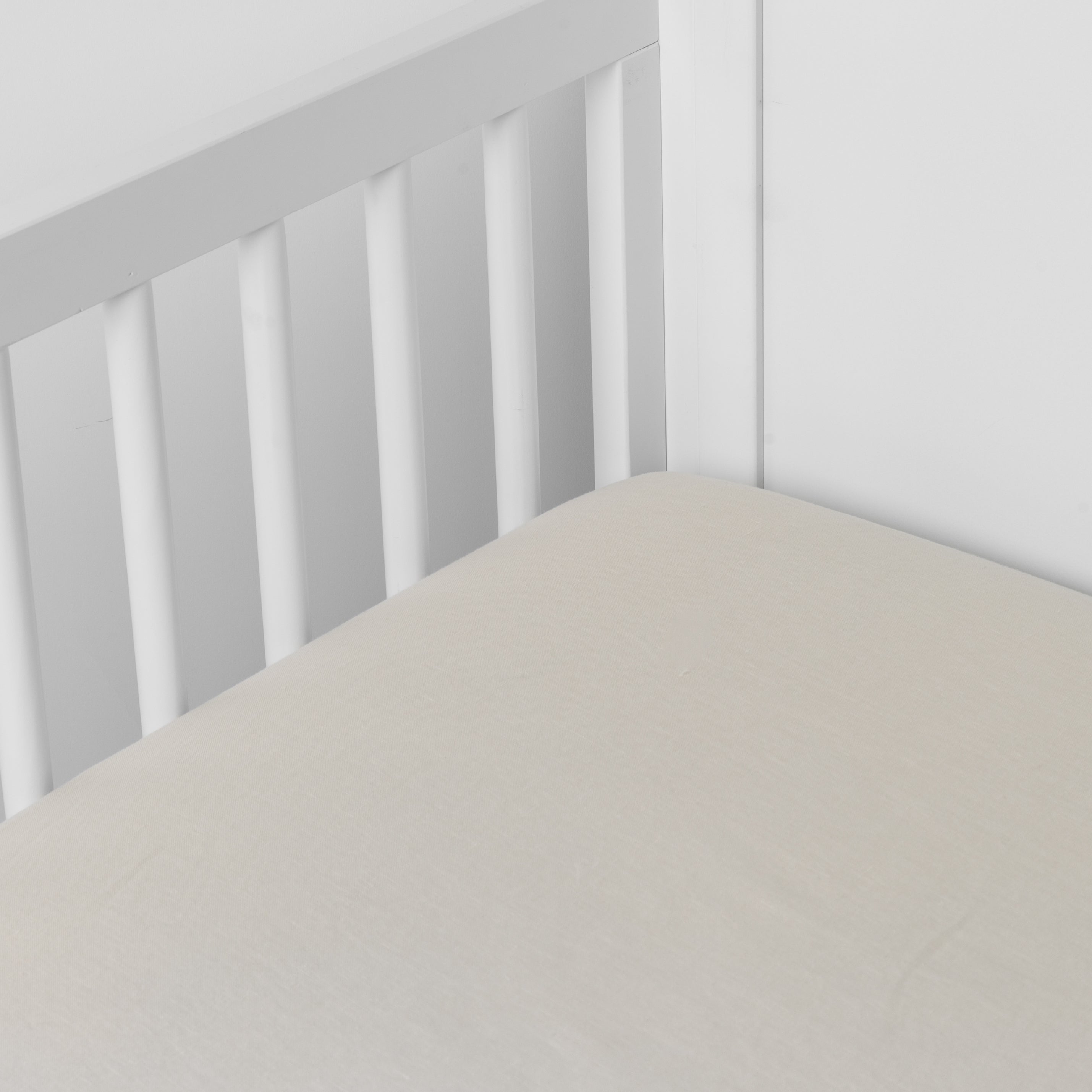 Parchment: linen crib sheet on the mattress shot slightly overhead into the corner of a white crib. against a white background.