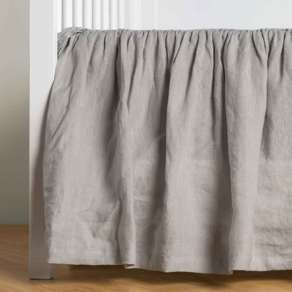 Cloud: crib skirt shown on a white crib with no mattress against a white wall and medium wood flooring.