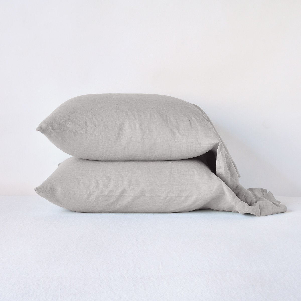 : Two linen slepping pillows in fog, stacked neatly against a plain background - side view.