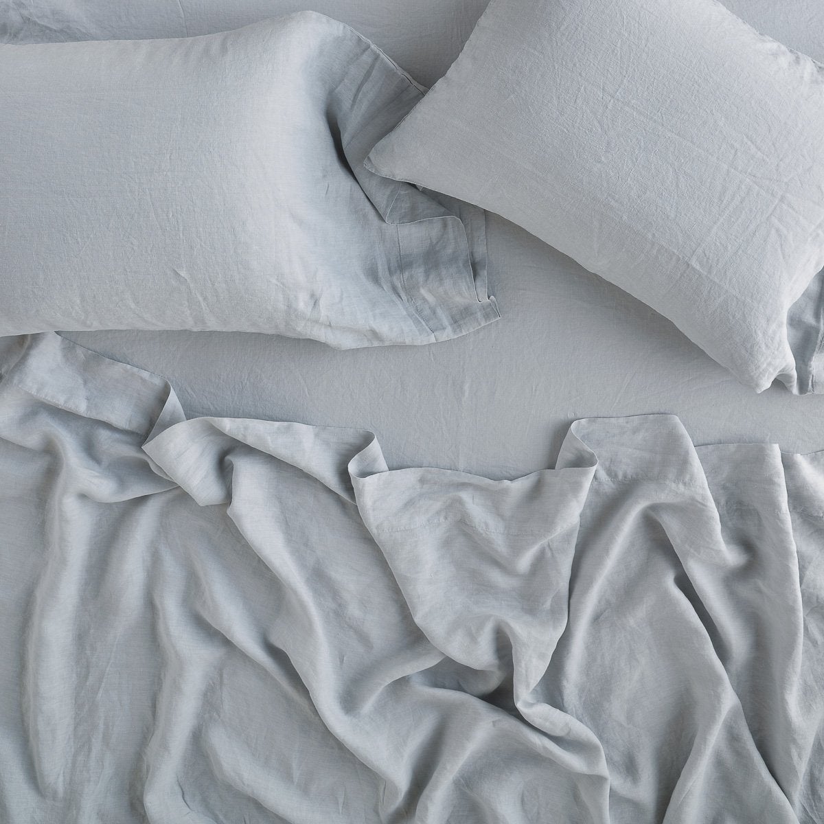 : Linen sleeping pillows in mineral, laid flat on matching sheeting - overhead view.