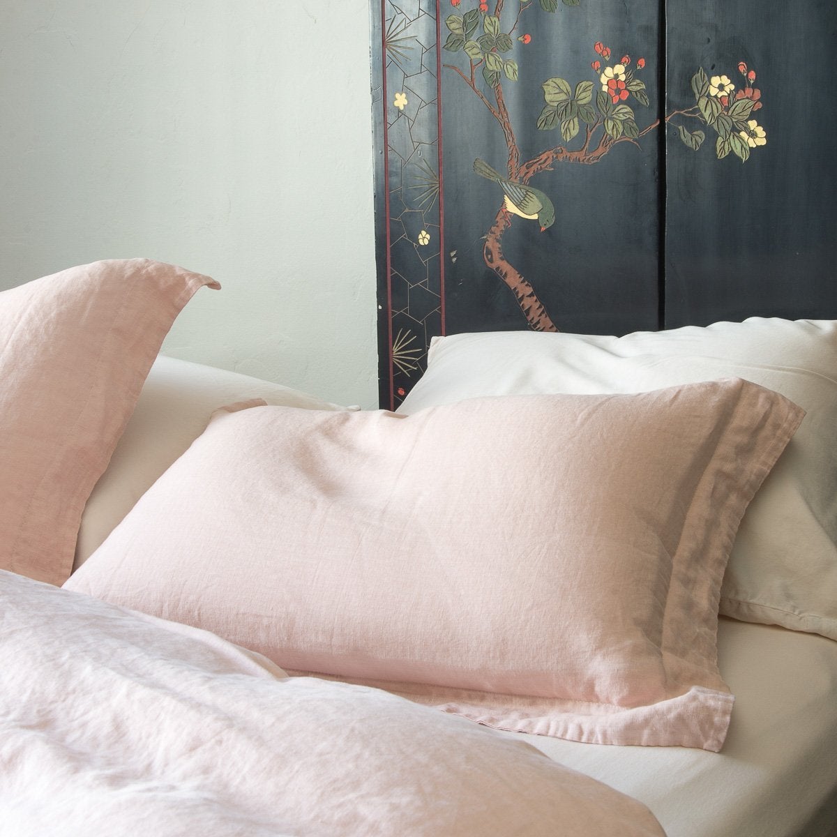 : Close-up linen sham in pearl over white sheeting, highlighting simple yet elegant self flange - cropped three-quarter angle.