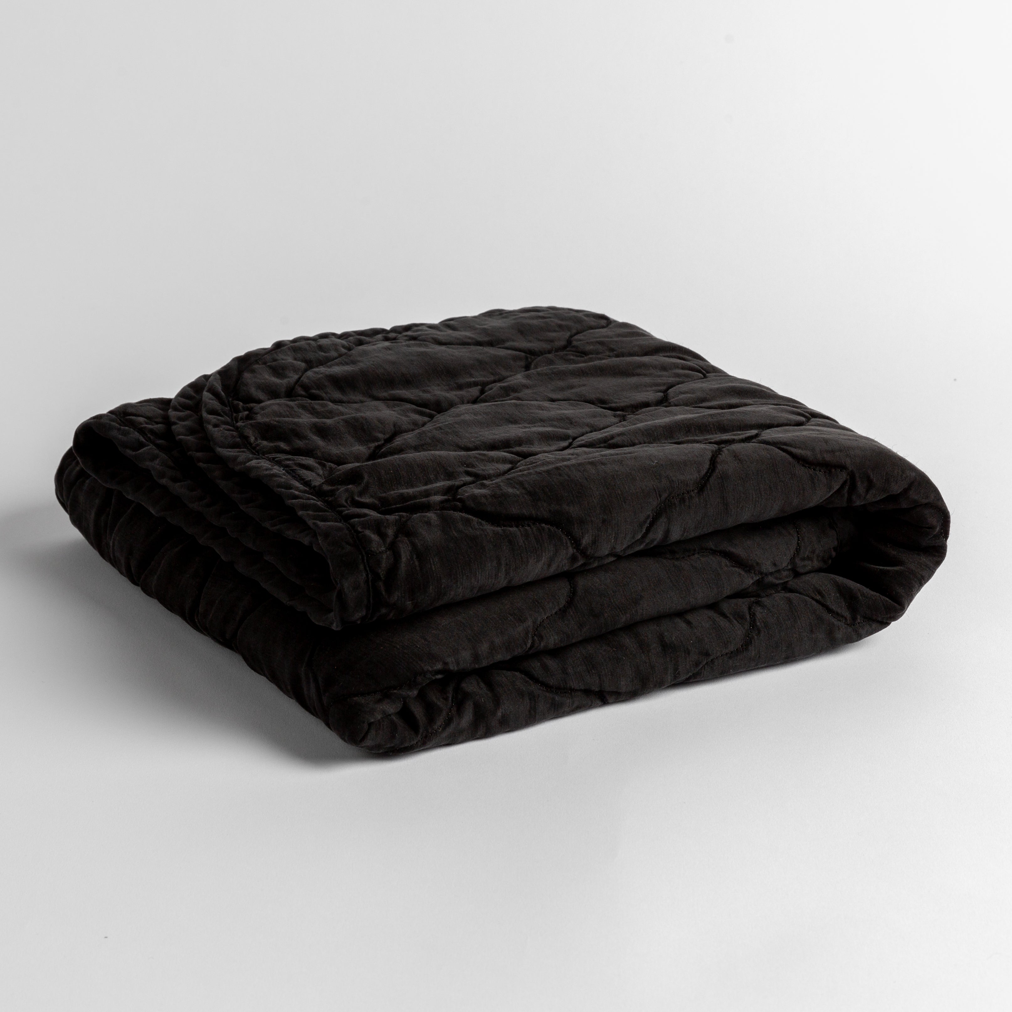 Corvino: quilted charmeuse blanket folded and shown against a white background from a slight overhead angle.