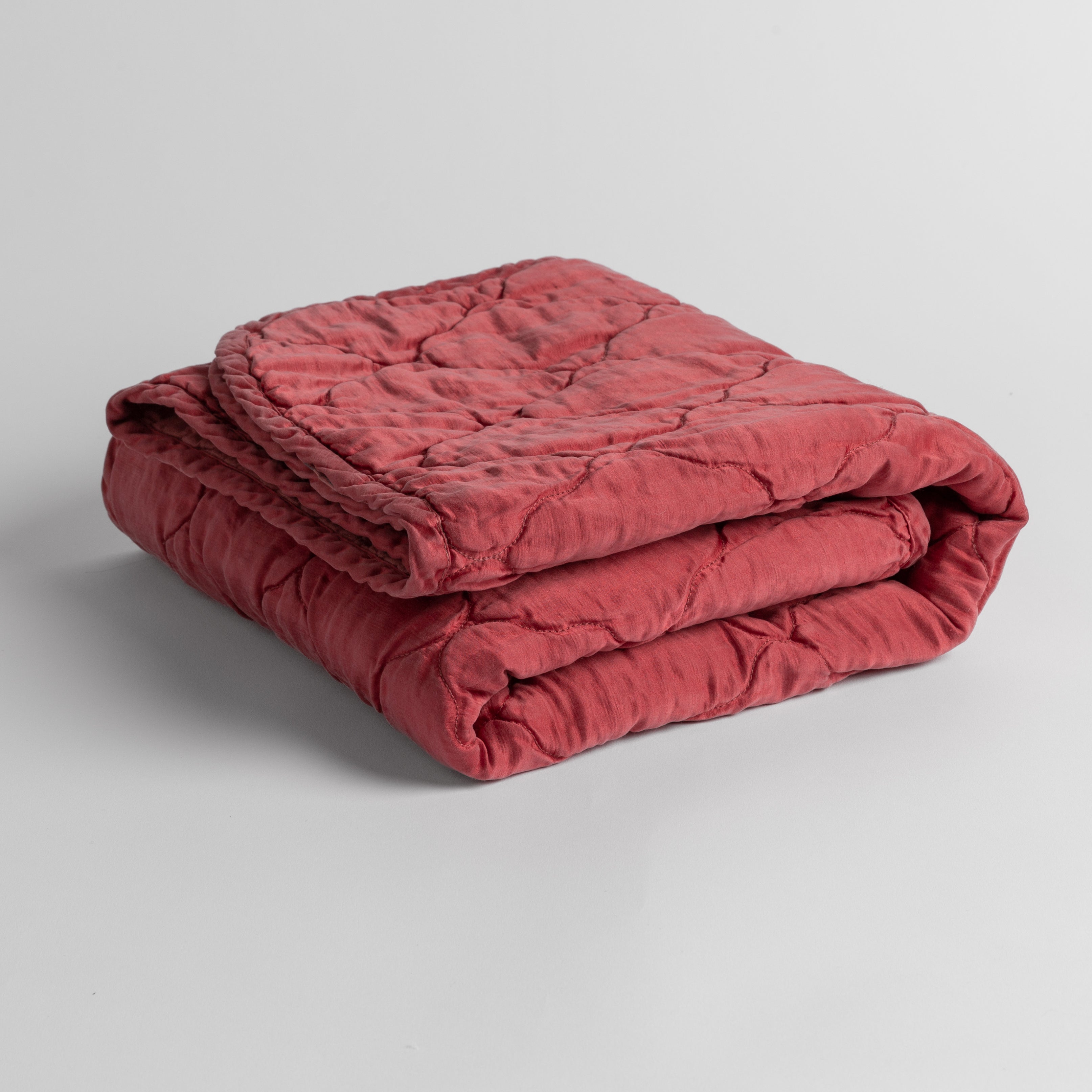 Poppy: quilted charmeuse blanket folded and shown against a white background from a slight overhead angle.