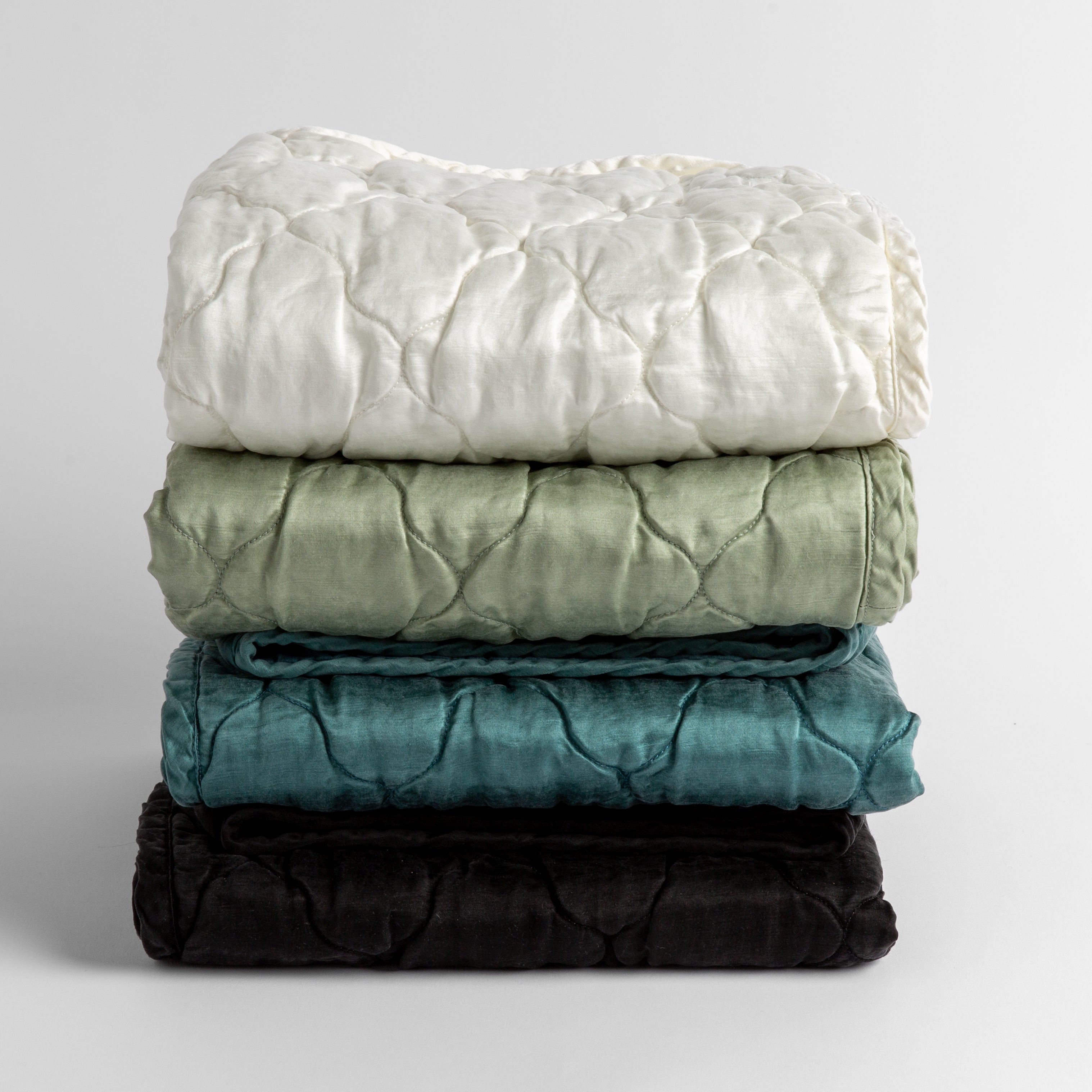 : a stack of four quilted silk charmeuse baby blankets shown straight on against a white background. Blankets shown in Winter White, Eucalyptus, Cenote and Corvino.