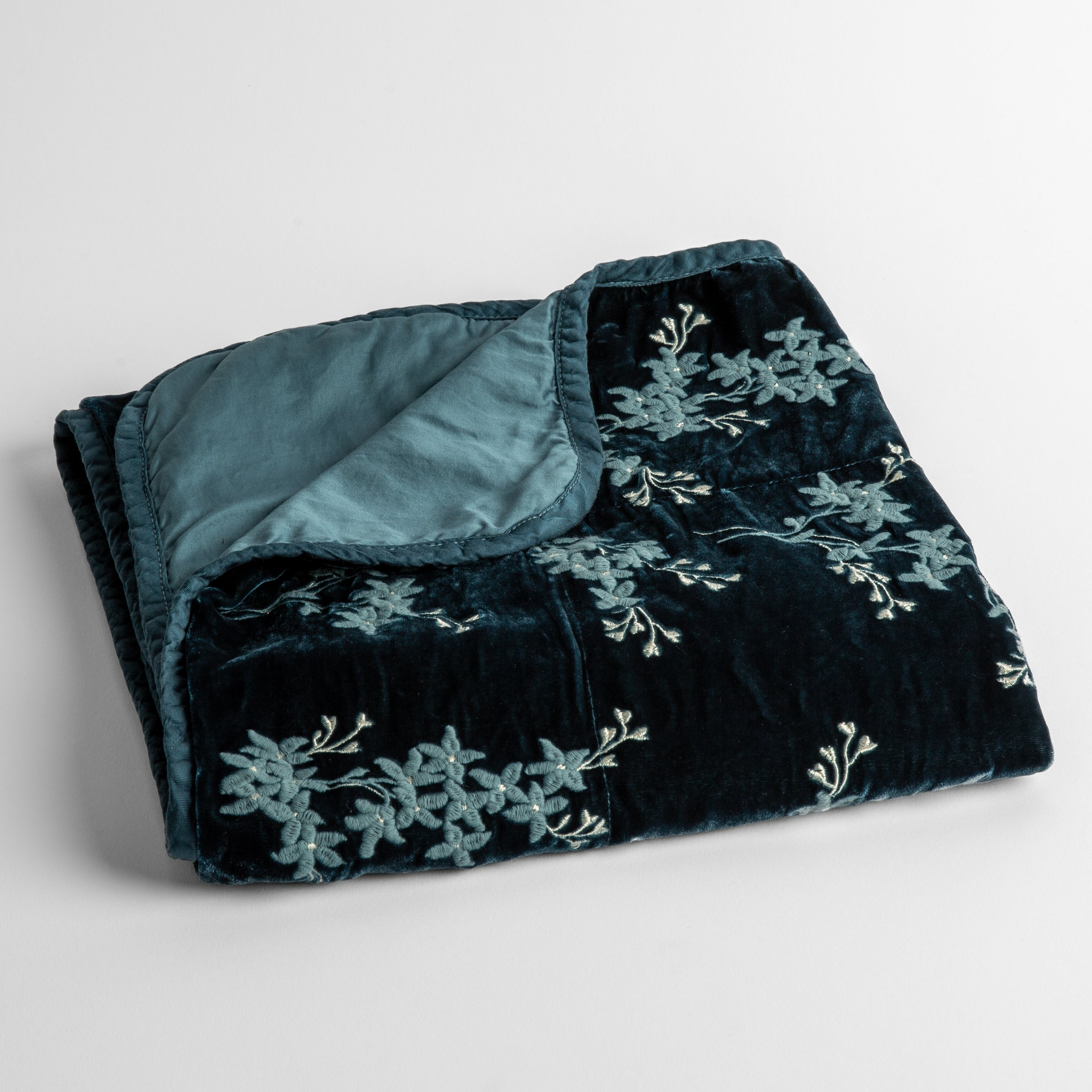 Cenote: embroidered silk velvet baby blanket folded with a corner folded back to show the trim and back of the blanket - shot overhead at a slight angle against a white background.