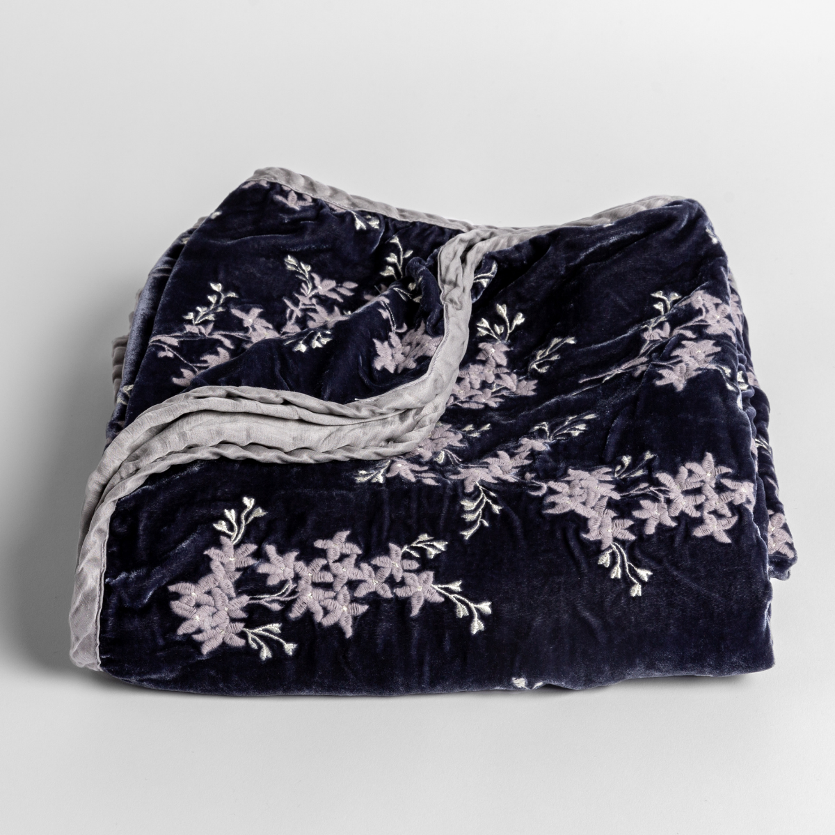 French Lavender: embroidered silk velvet blanket folded with corners folded down to show the trim detail - slightly overhead against a white background.