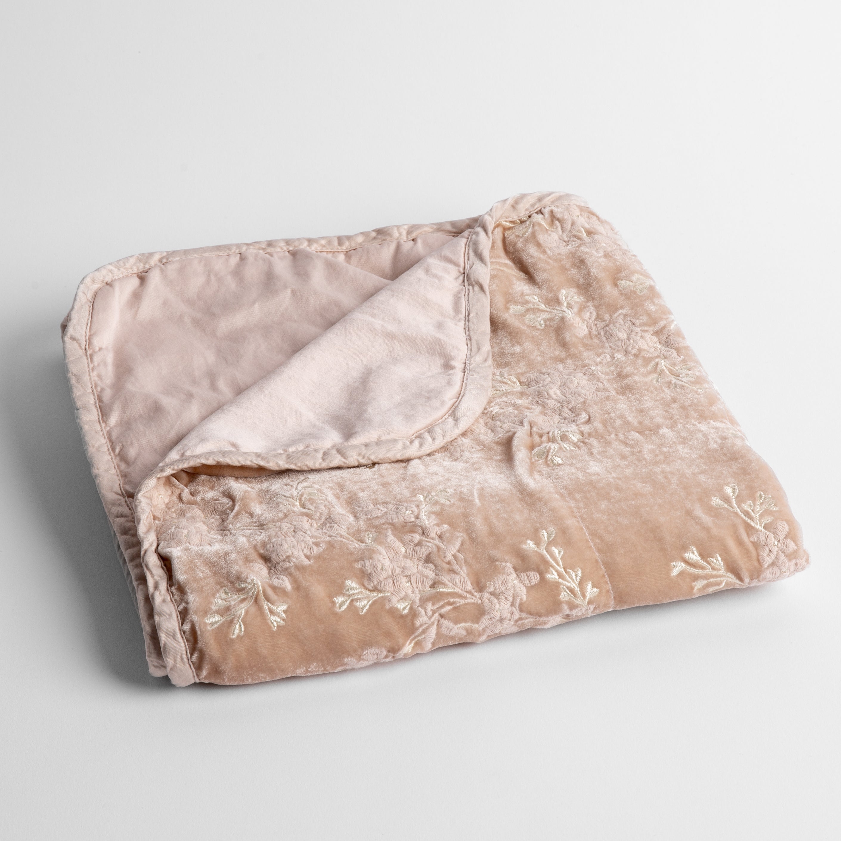 Pearl: embroidered silk velvet baby blanket folded with a corner folded back to show the trim and back of the blanket - shot overhead at a slight angle against a white background.