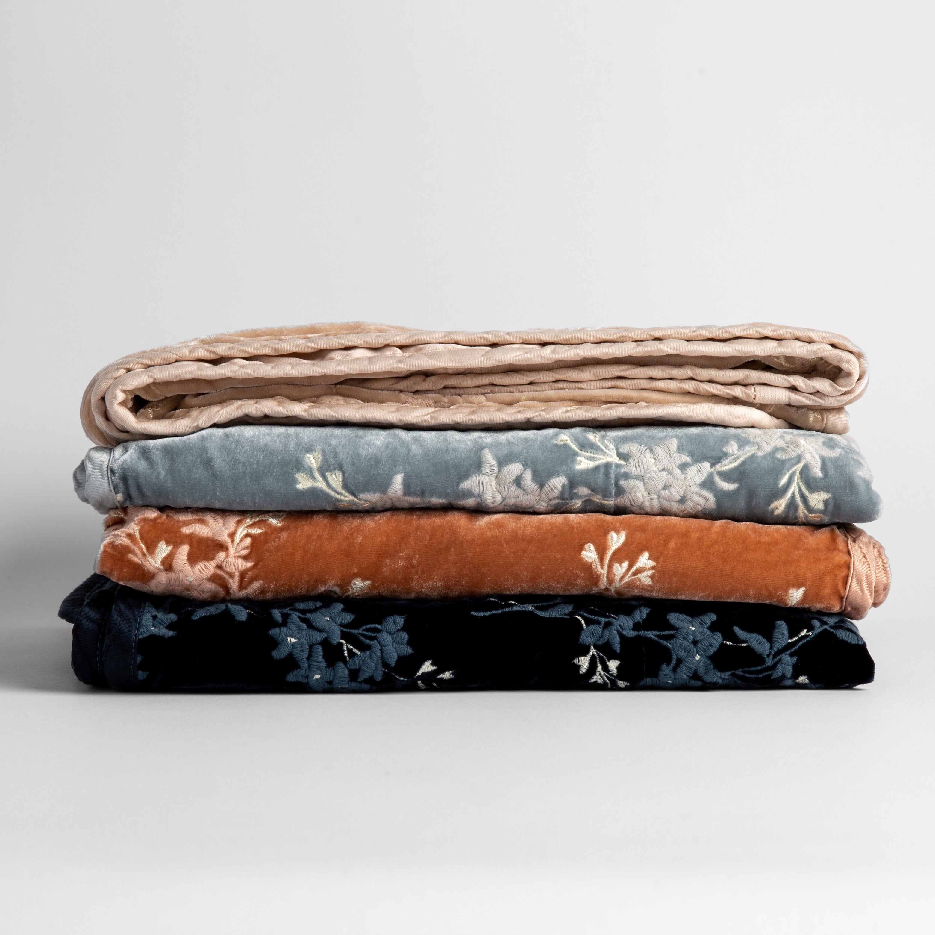 : stack of embroidered silk velvet baby blankets shot against a white background.