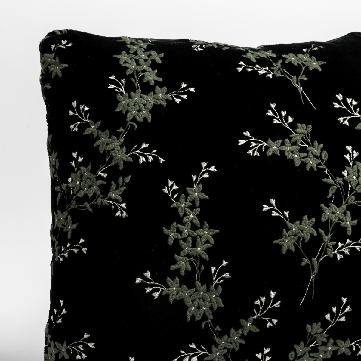 Close up of the corner of a floral embroidery patterned silk velvet pillow cushion in Juniper, a dark green tone.