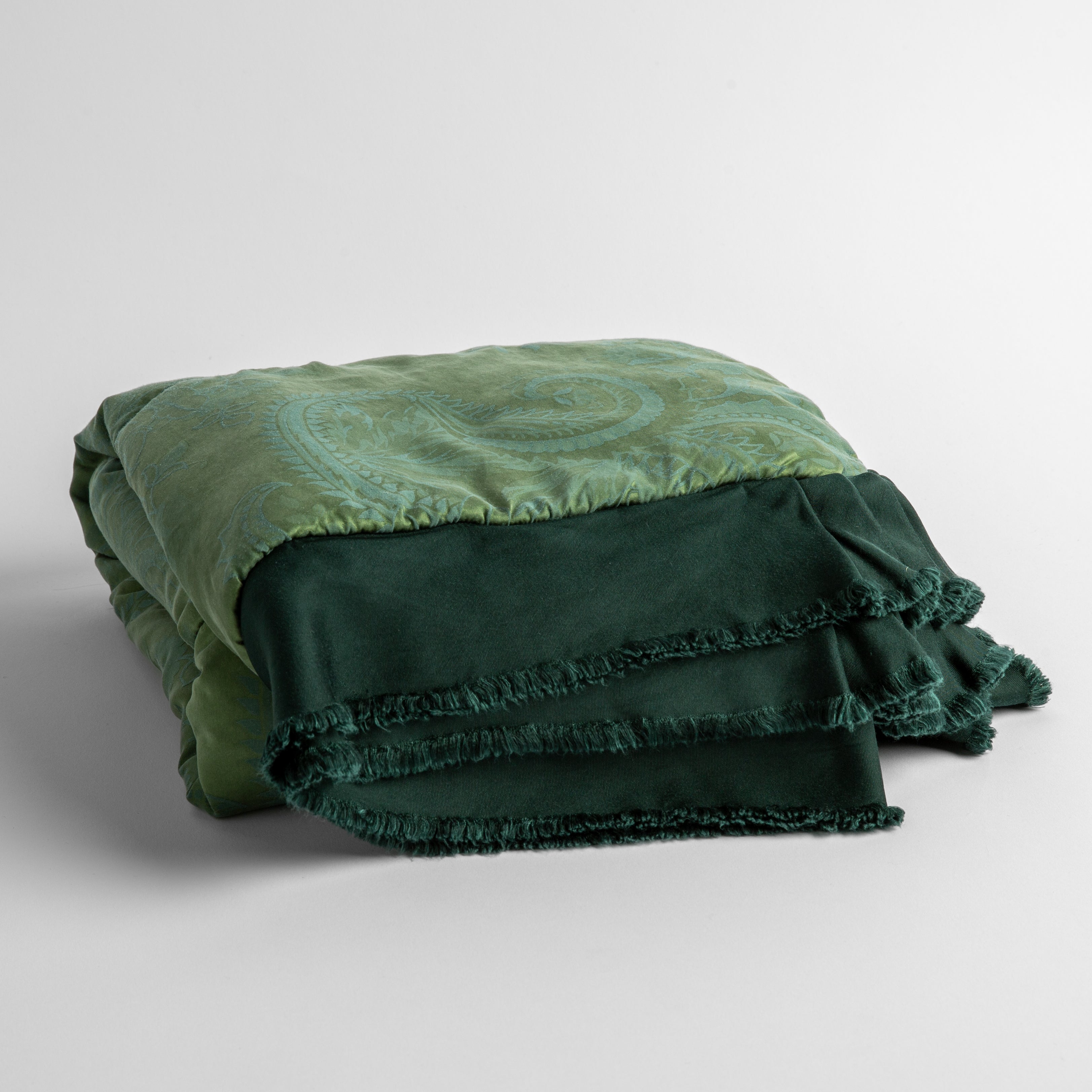 A folded baby blanket in Jade with its raw-edged ruffle shown in the forefront; Jade is a dark jewel-toned green shade.