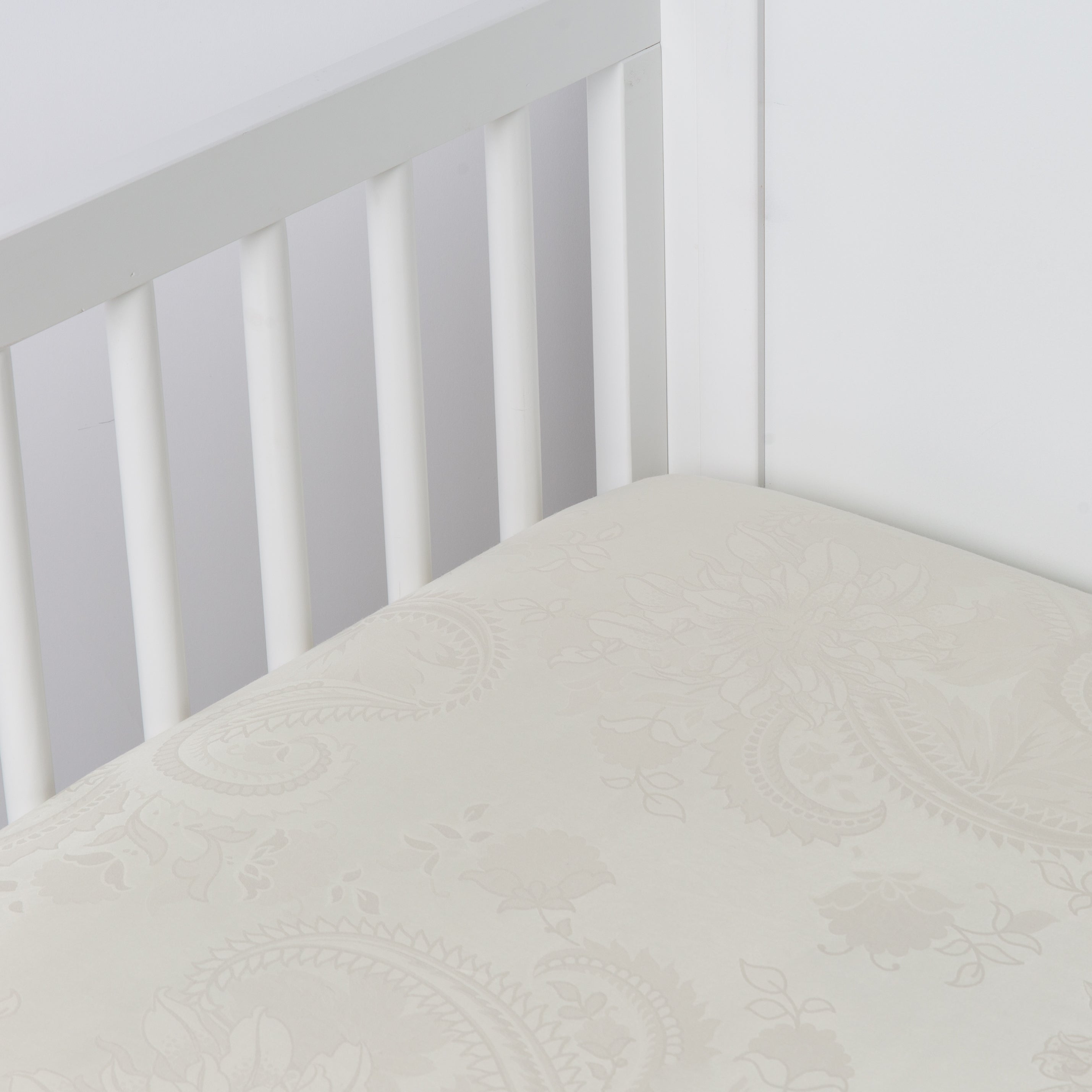 Parchment: silk and tencel™ blend jacquard crib sheet shot from above at a slight angle into the corner of a white crib.
