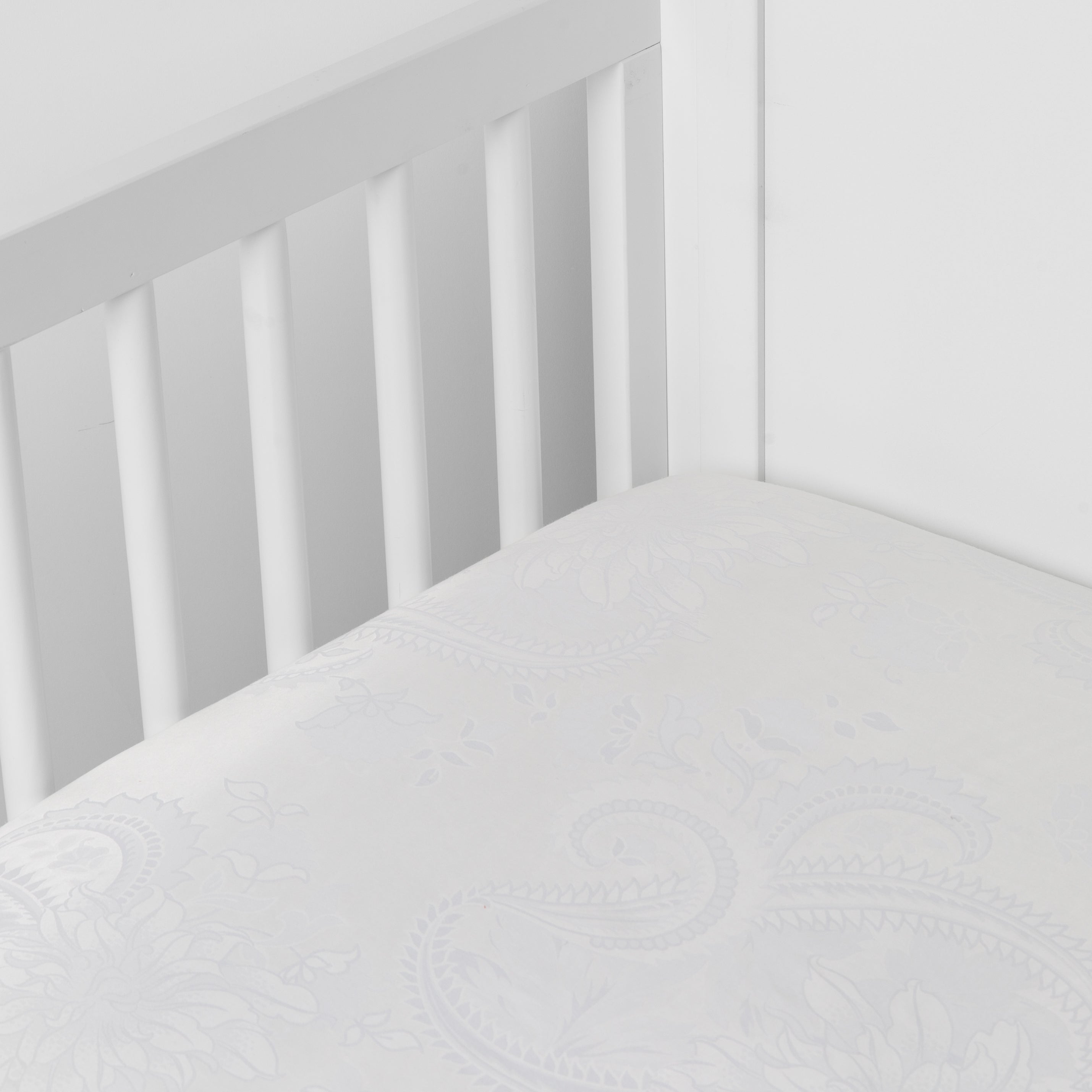 White: silk and tencel™ blend jacquard crib sheet shot from above at a slight angle into the corner of a white crib.
