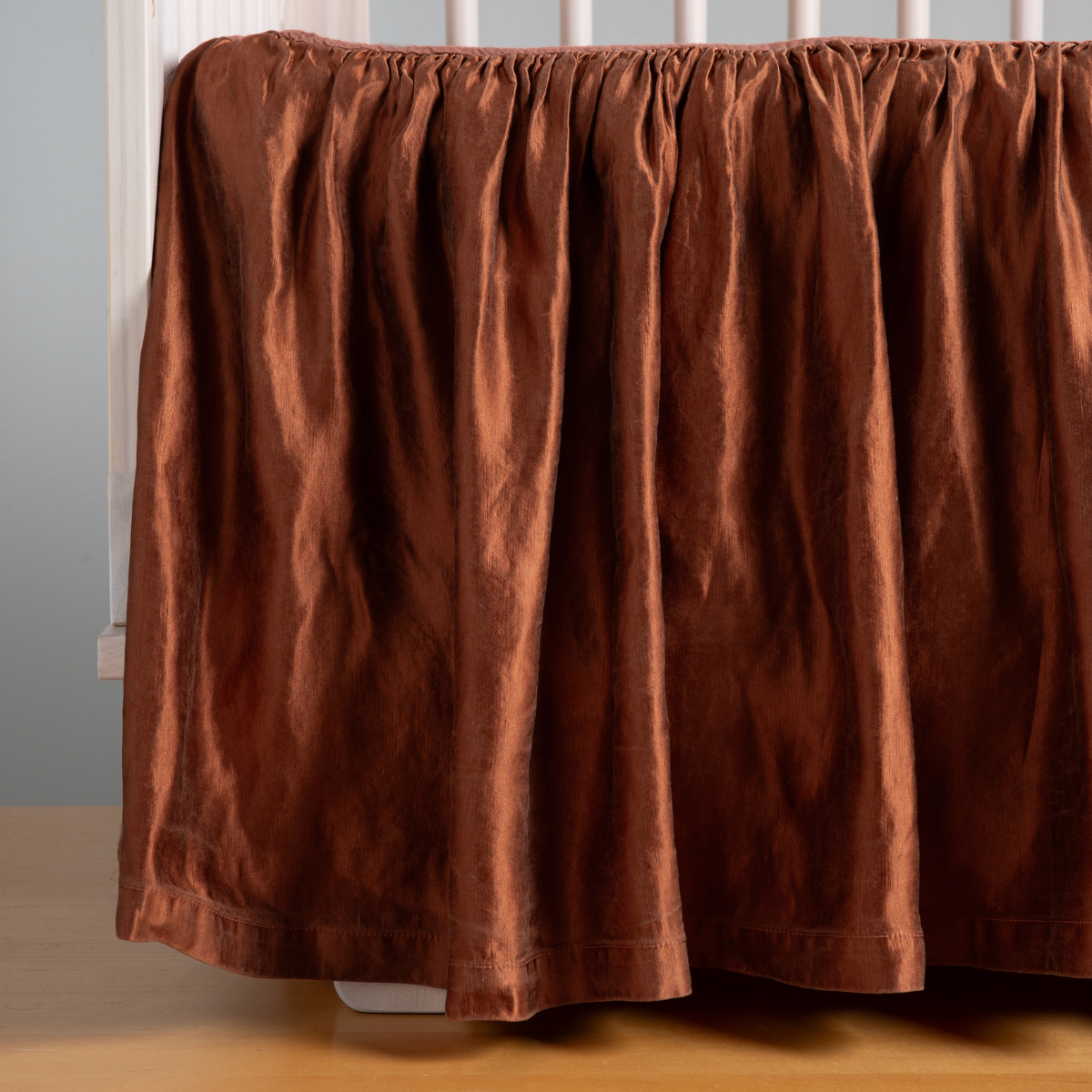 Autumn: A close-up side view of a crib with the Paloma crib skirt in Autumn, a rich terracotta tone.