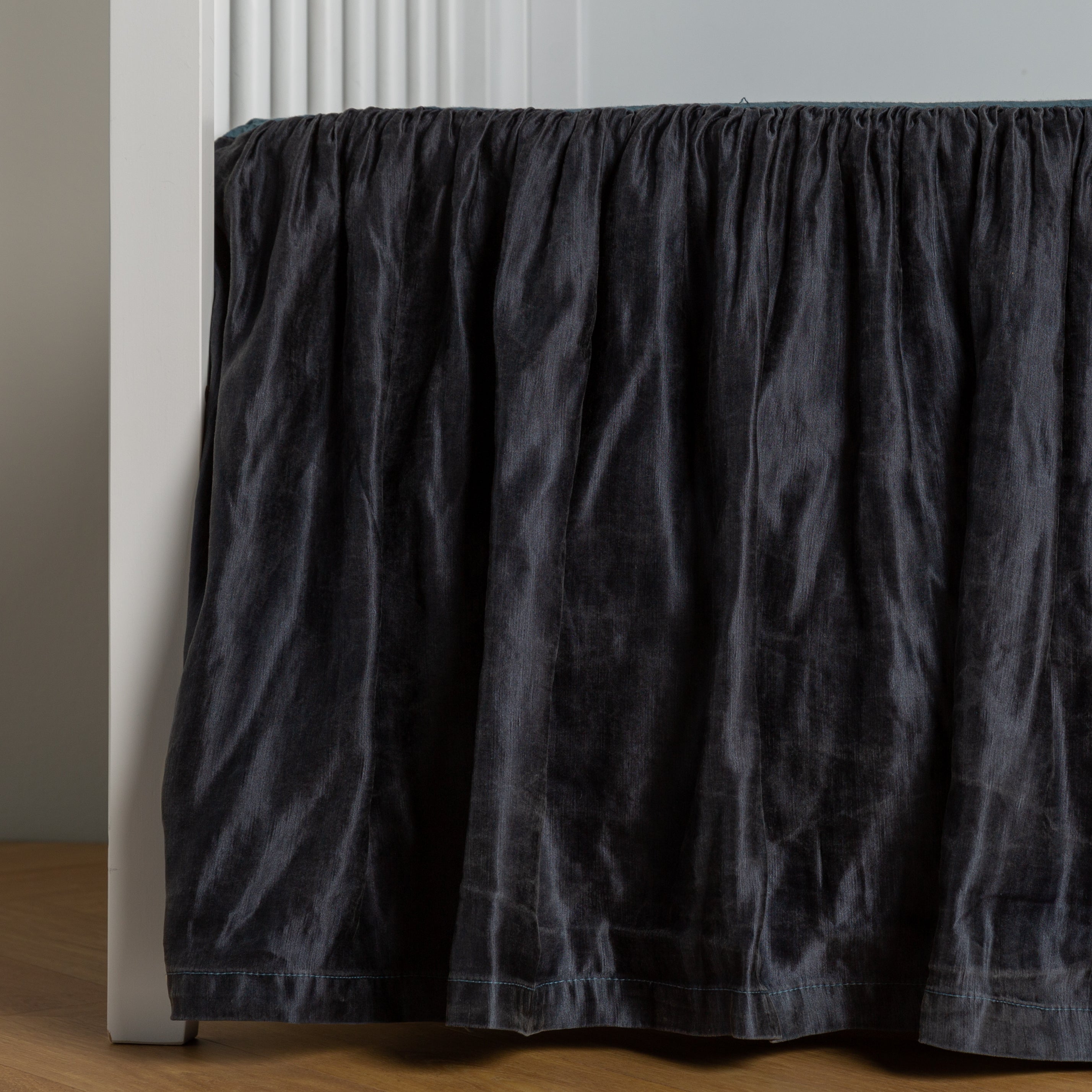 Midnight: charmeuse crib skirt shown on a white crib against a white wall and medium wood floor.