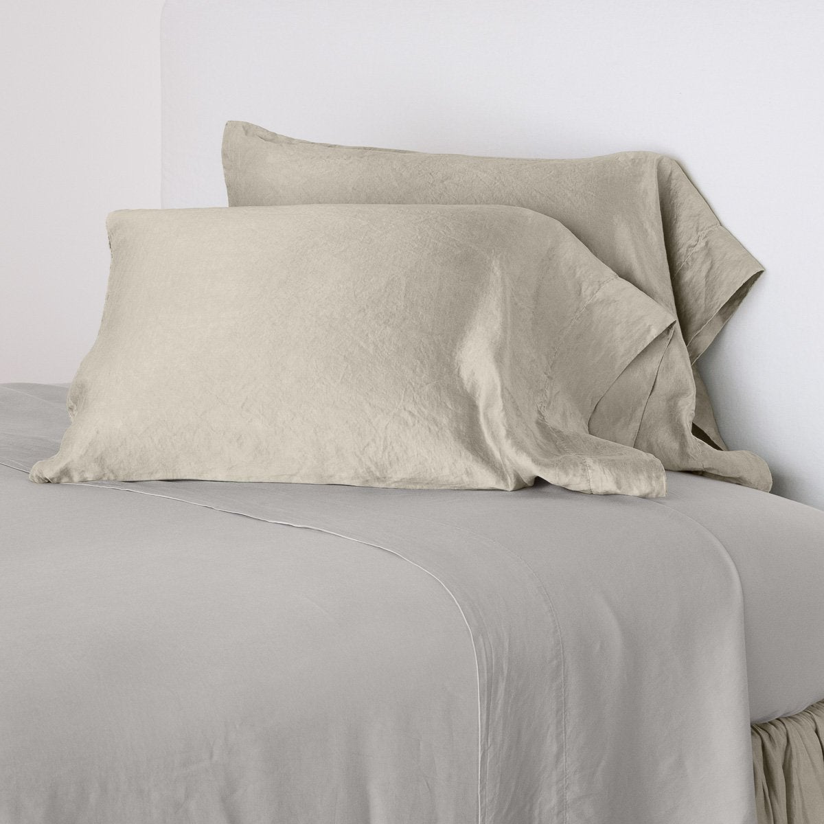 Fog: sleeping pillows leaning upright against a white wall on monochromatic sheeting - cropped three-quarter angle.