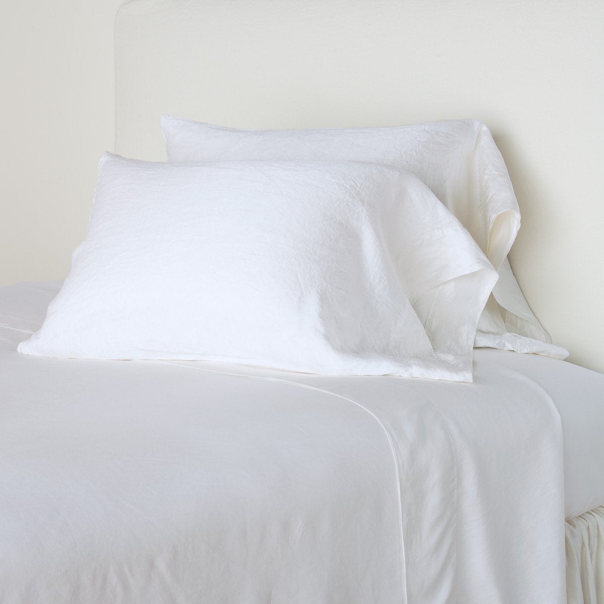White: sleeping pillows leaning upright against a white wall on monochromatic sheeting - cropped three-quarter angle.