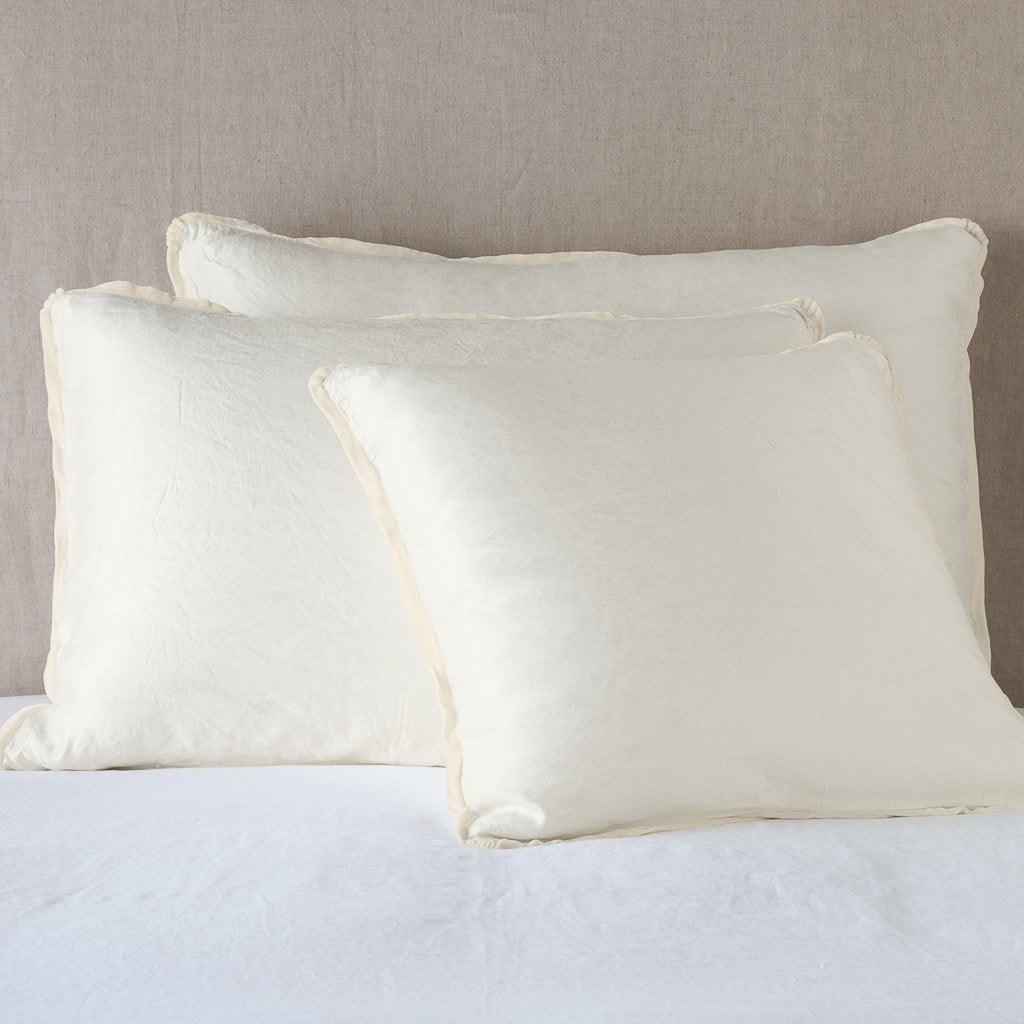 Parchment: shams leaning upright on white sheeting against a neutral headboard.